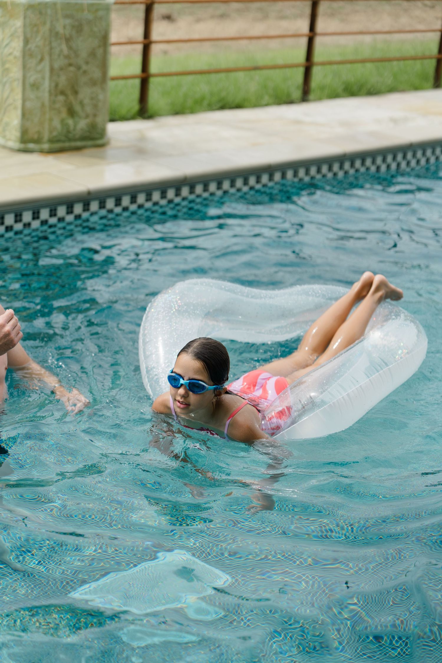 Young girl with goggles relaxing on inflatable ring float in outdoor swimming pool.