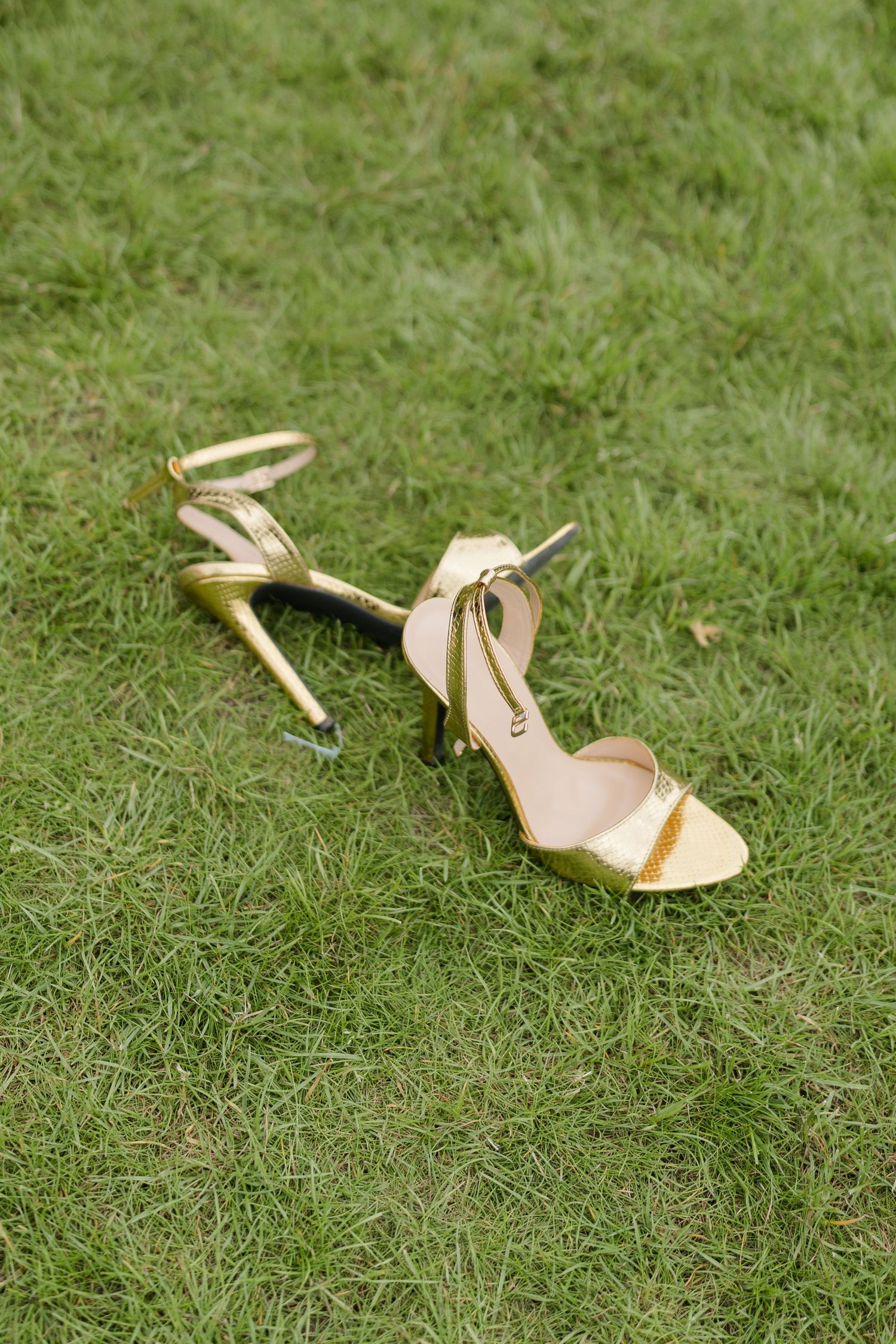 Gold strappy high heel sandals resting on green grass at a wedding reception.