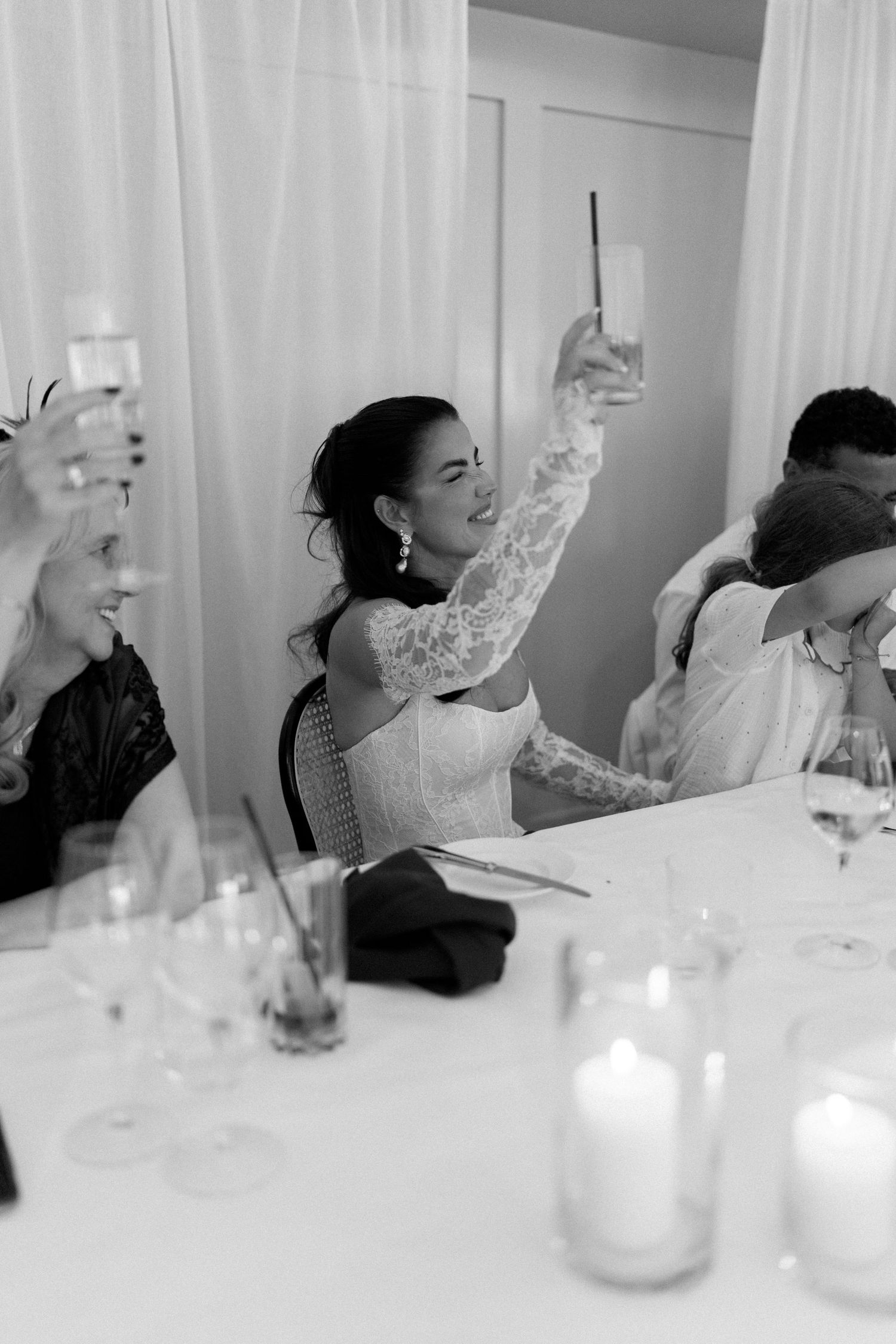 A black and white photo of a bride raising a champagne glass during a wedding reception toast.