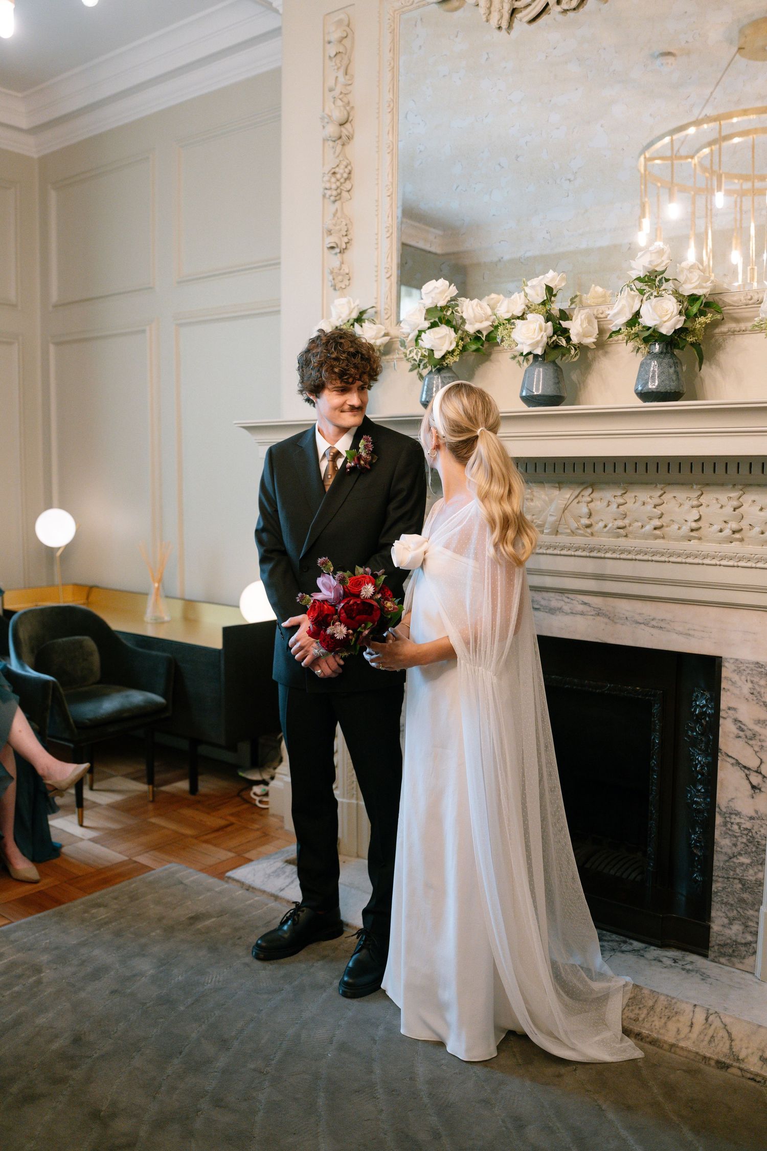 Wedding ceremony in a classic white room with a decorative fireplace mantle.