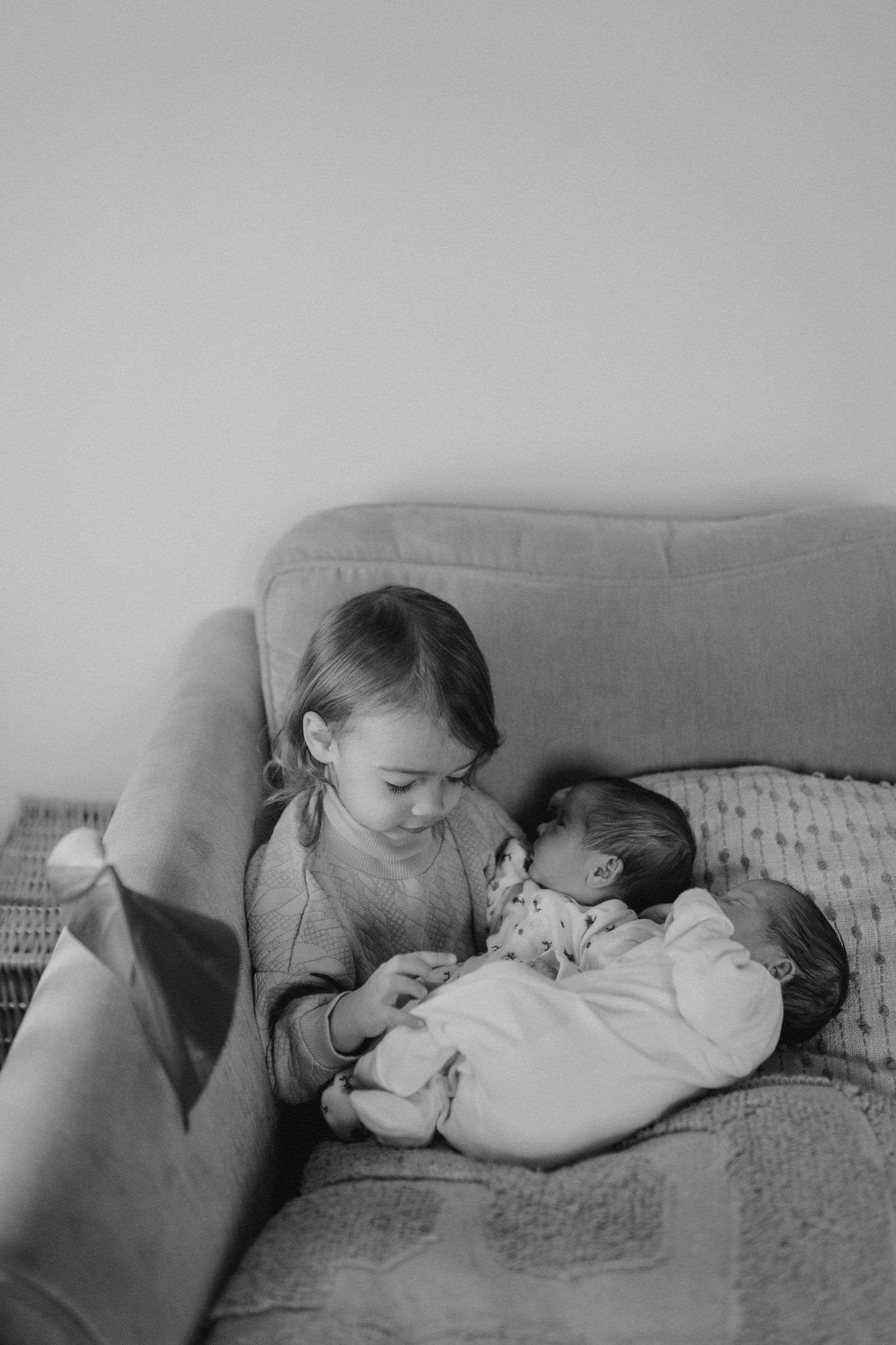 Two small children share an affectionate moment on a grey couch.