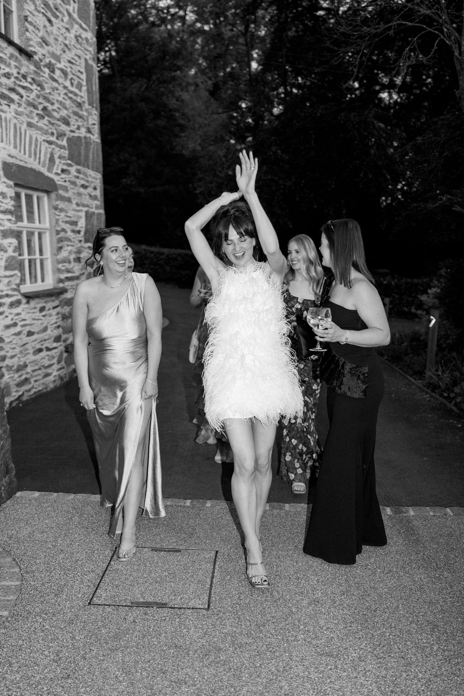 Friends celebrating at a party outside a stone building, with one person in a white feathered dress.