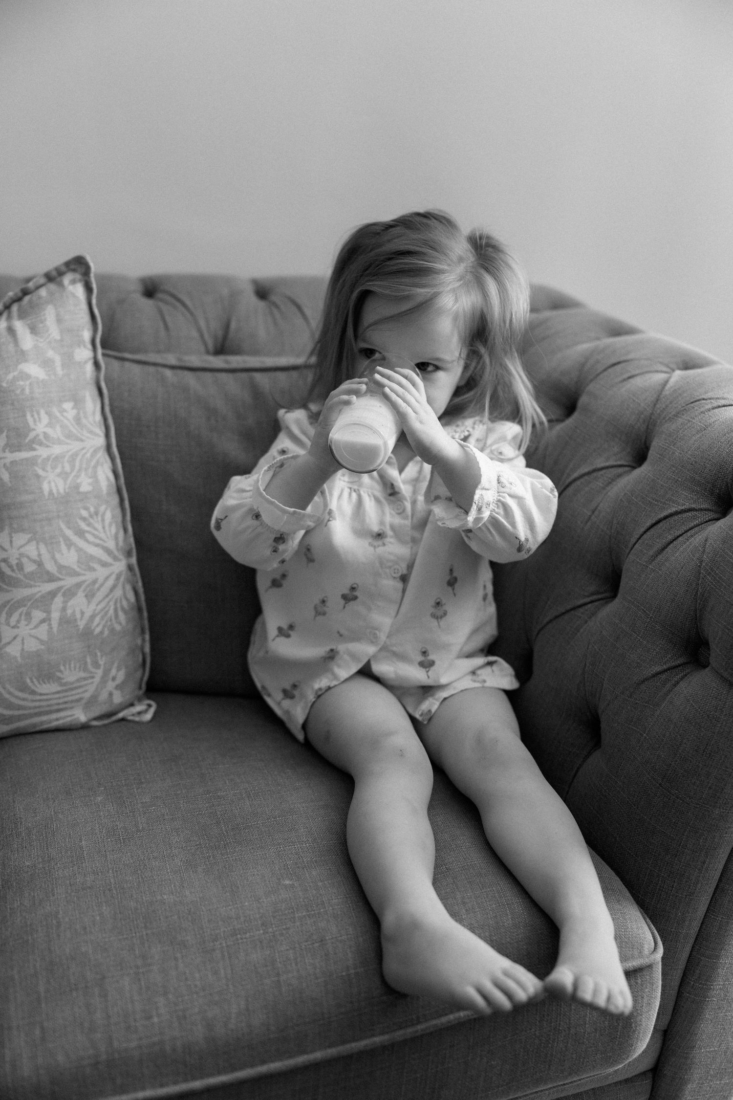 Small child relaxing on grey couch holding a cup.