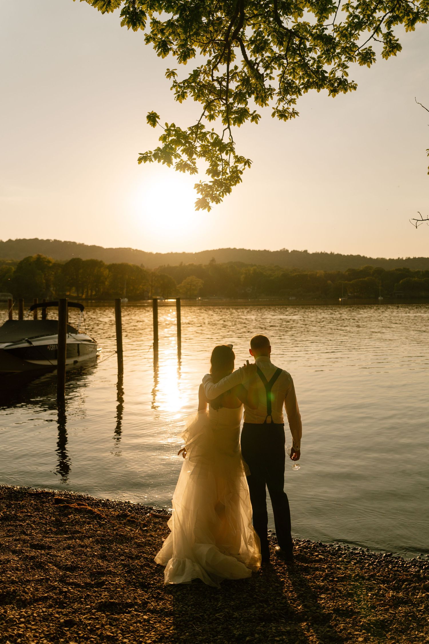 A romantic sunset silhouette by a lake with wooden posts and overhanging tree branches.