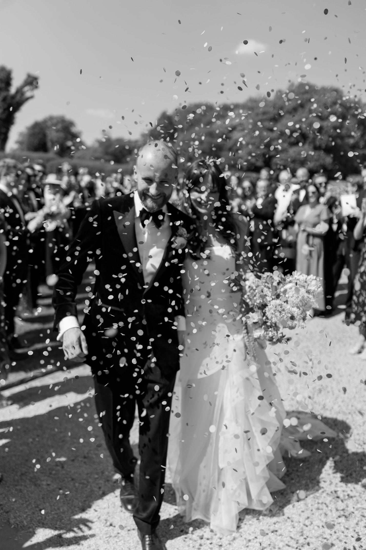 Black and white capture of confetti floating through the air during an outdoor wedding celebration.