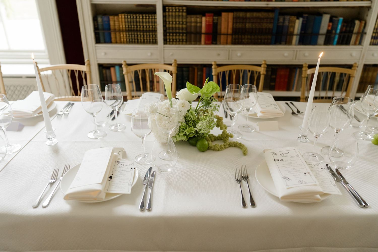 Elegant white wedding reception table set with candles, glassware, and floral centerpiece.