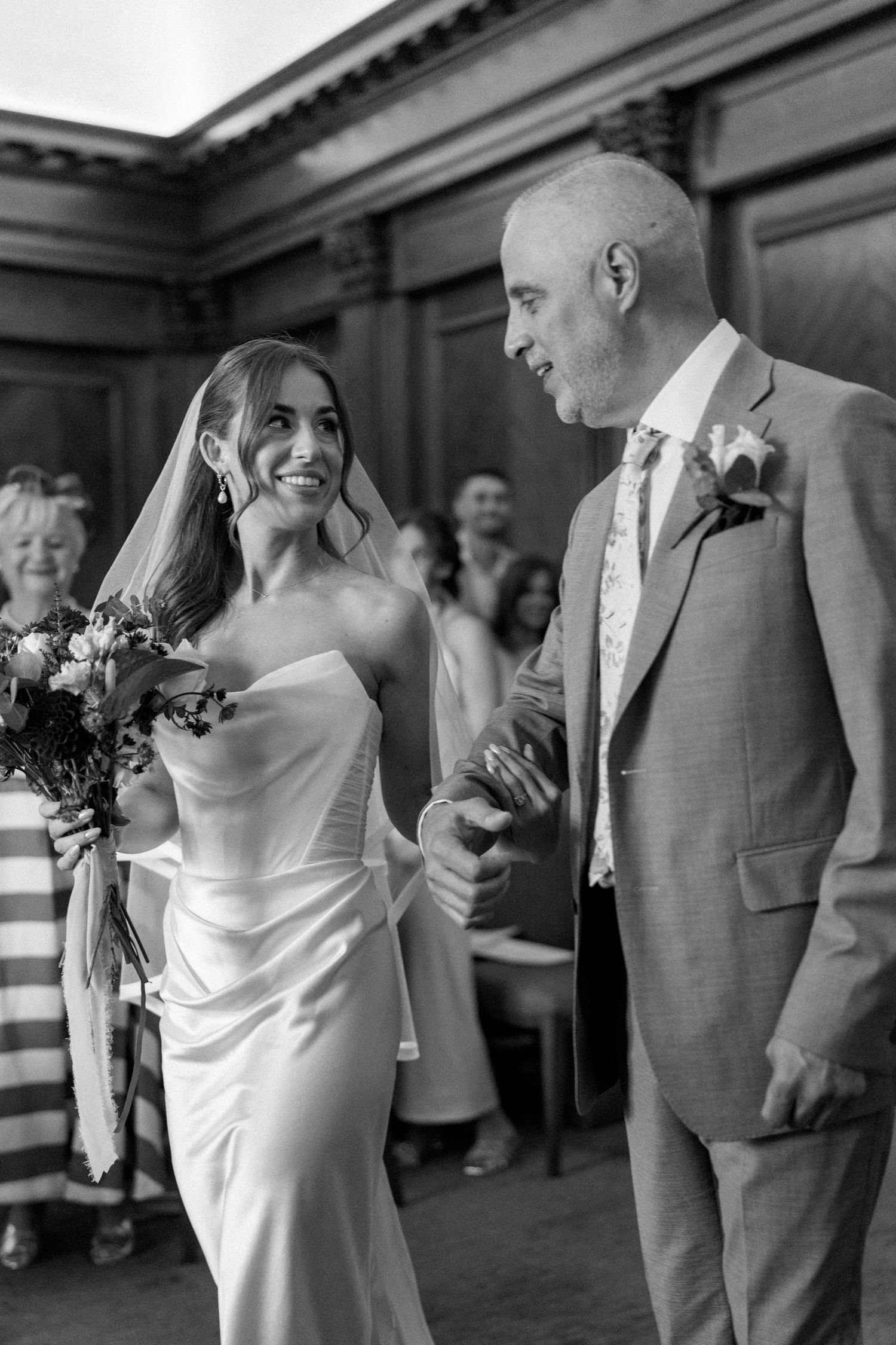 Bride and groom share a joyful moment walking together during their wedding ceremony in black and white.