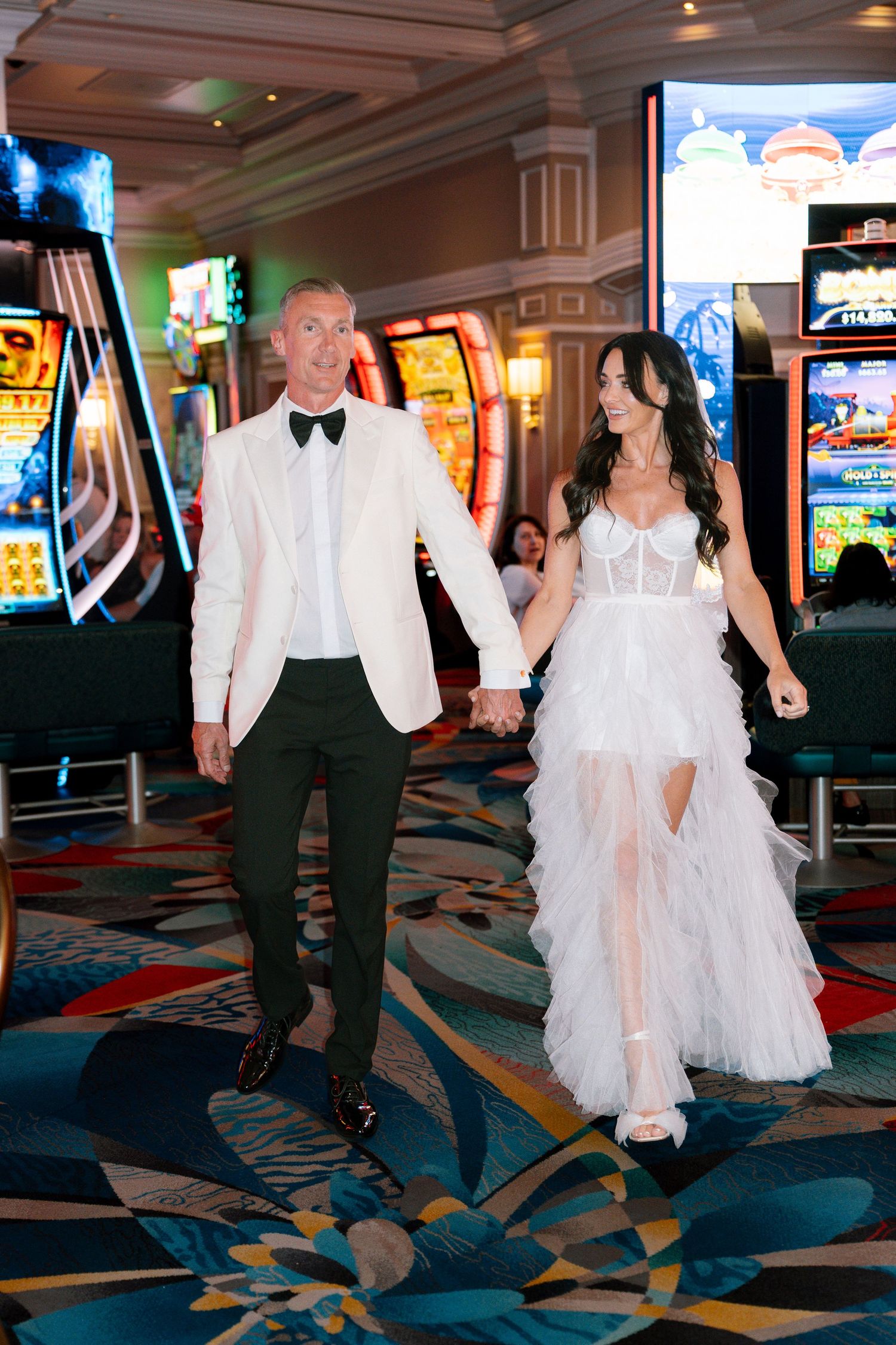 Bride and groom walk through a colorful casino floor during their wedding celebration.