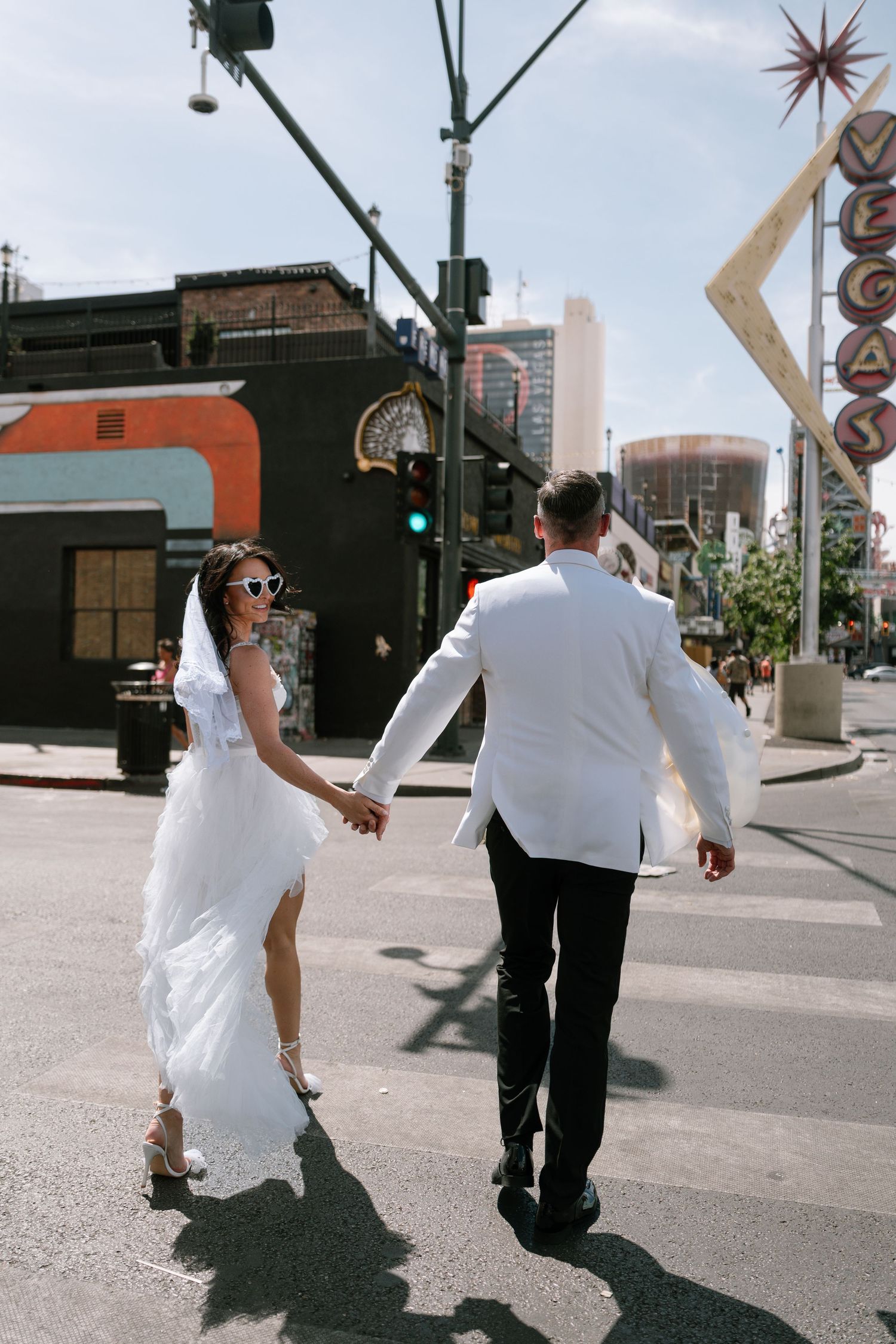A couple in formal attire walking down a city street with shadows casting on the pavement.