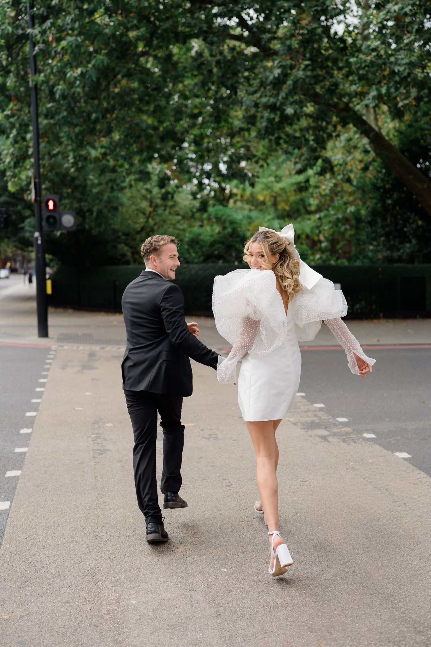 A couple in wedding attire playfully bending over on a city street.