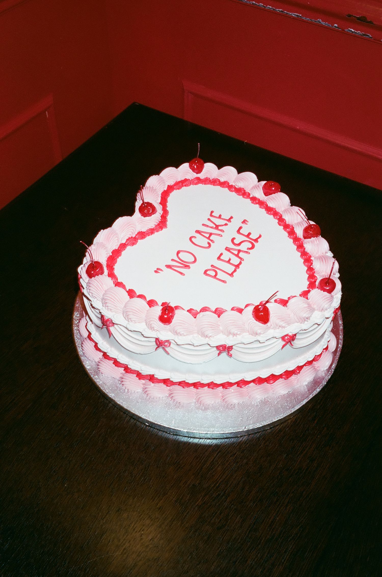 A white frosted cake with red trim and text displayed from different angles on a dark wooden surface.