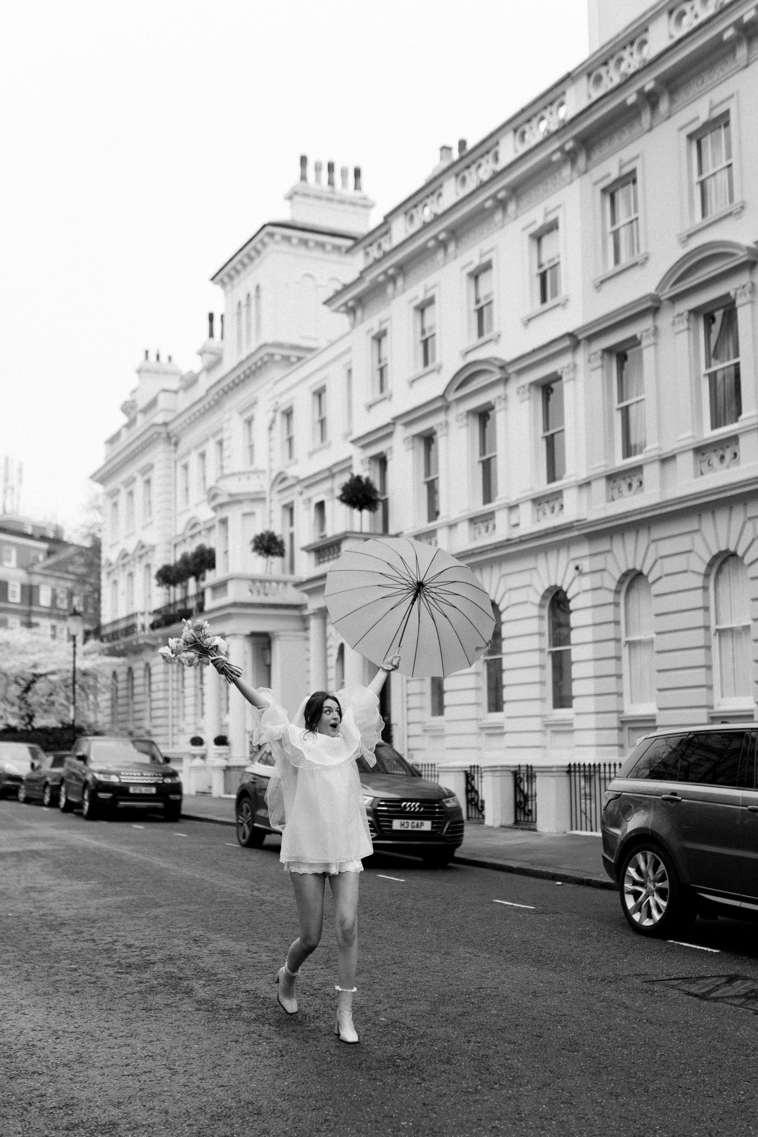 A person in white clothing walks with an umbrella along a classic London street lined with elegant white townhouses.