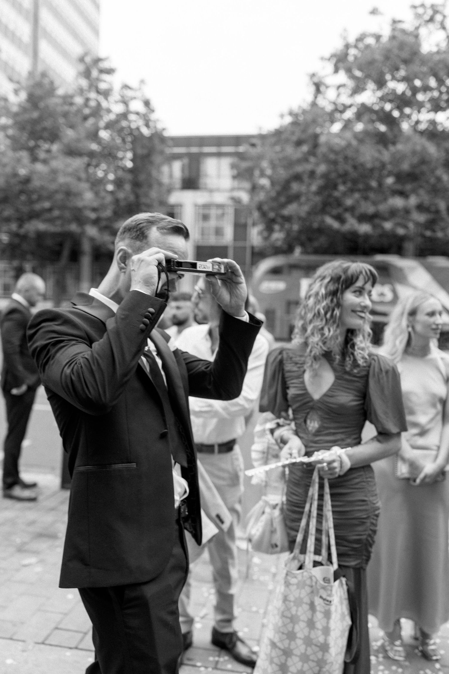 Wedding guests in formal attire gather outside for celebratory photos.