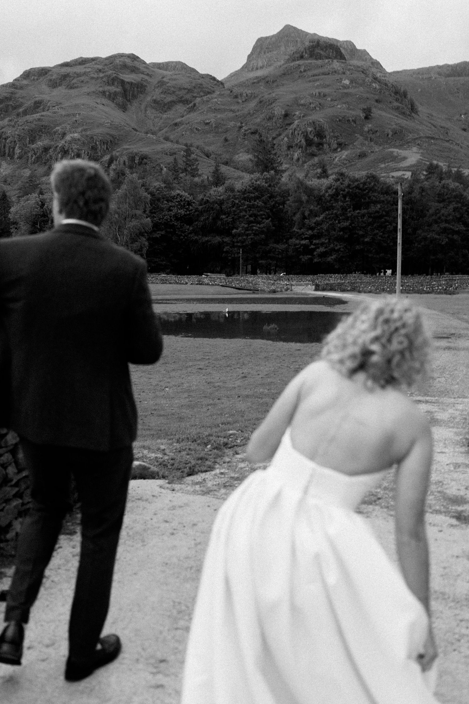 Wedding party walks through scenic mountain landscape on stone pathway.