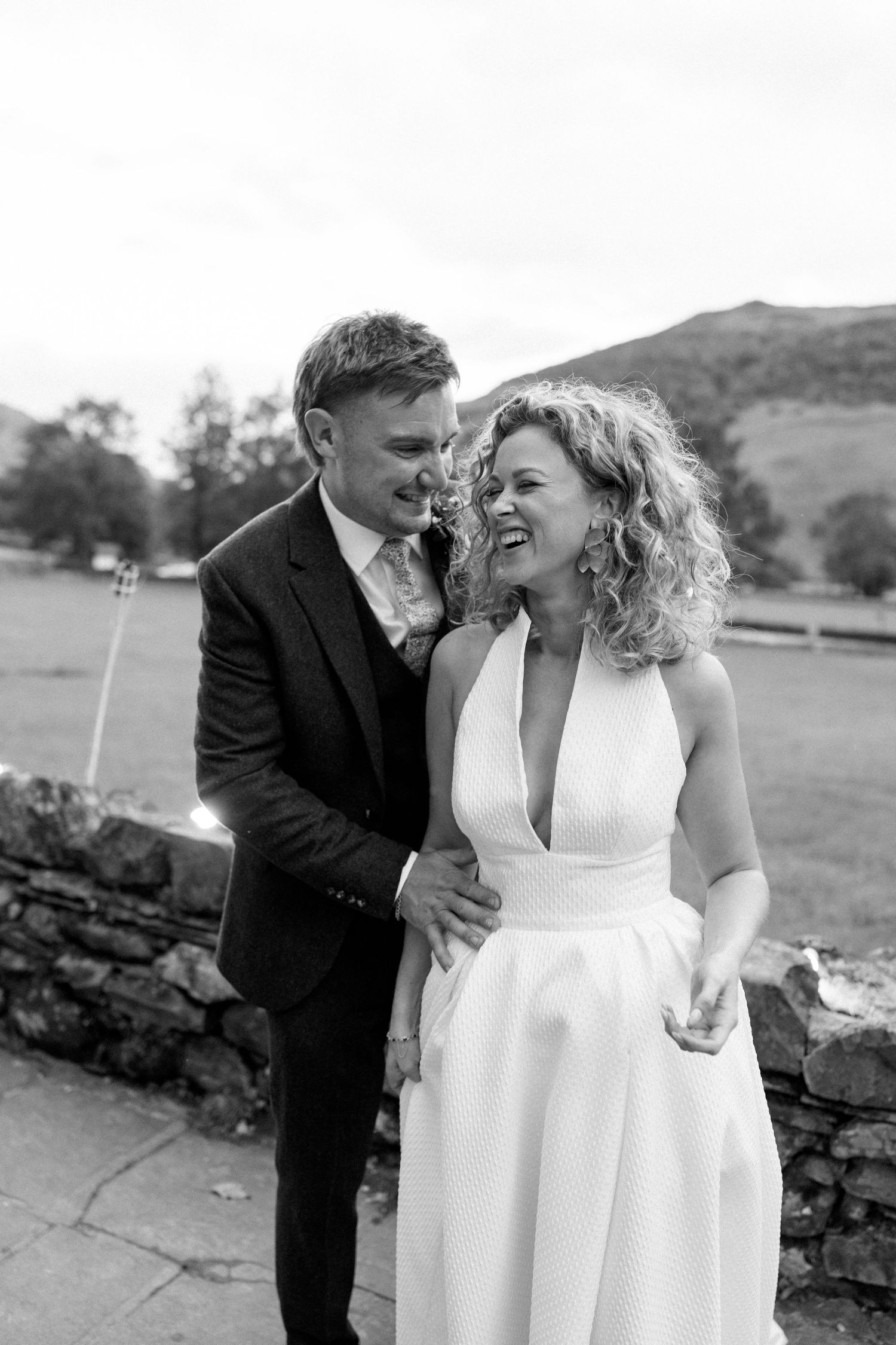 Candid black and white photo of joyful couple sharing laughter against rural landscape.