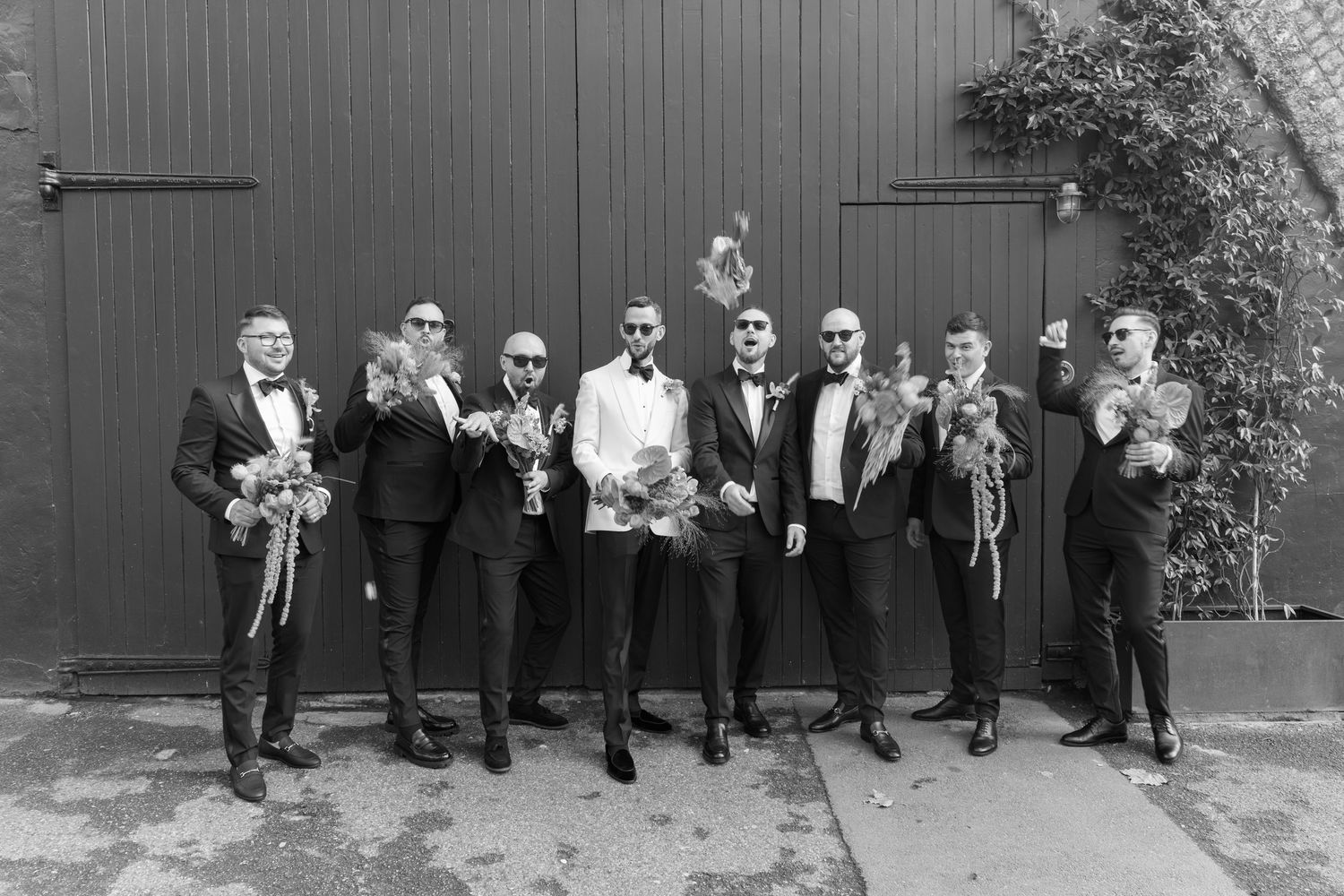 Groomsmen line up against grey wall for formal wedding party portraits.
