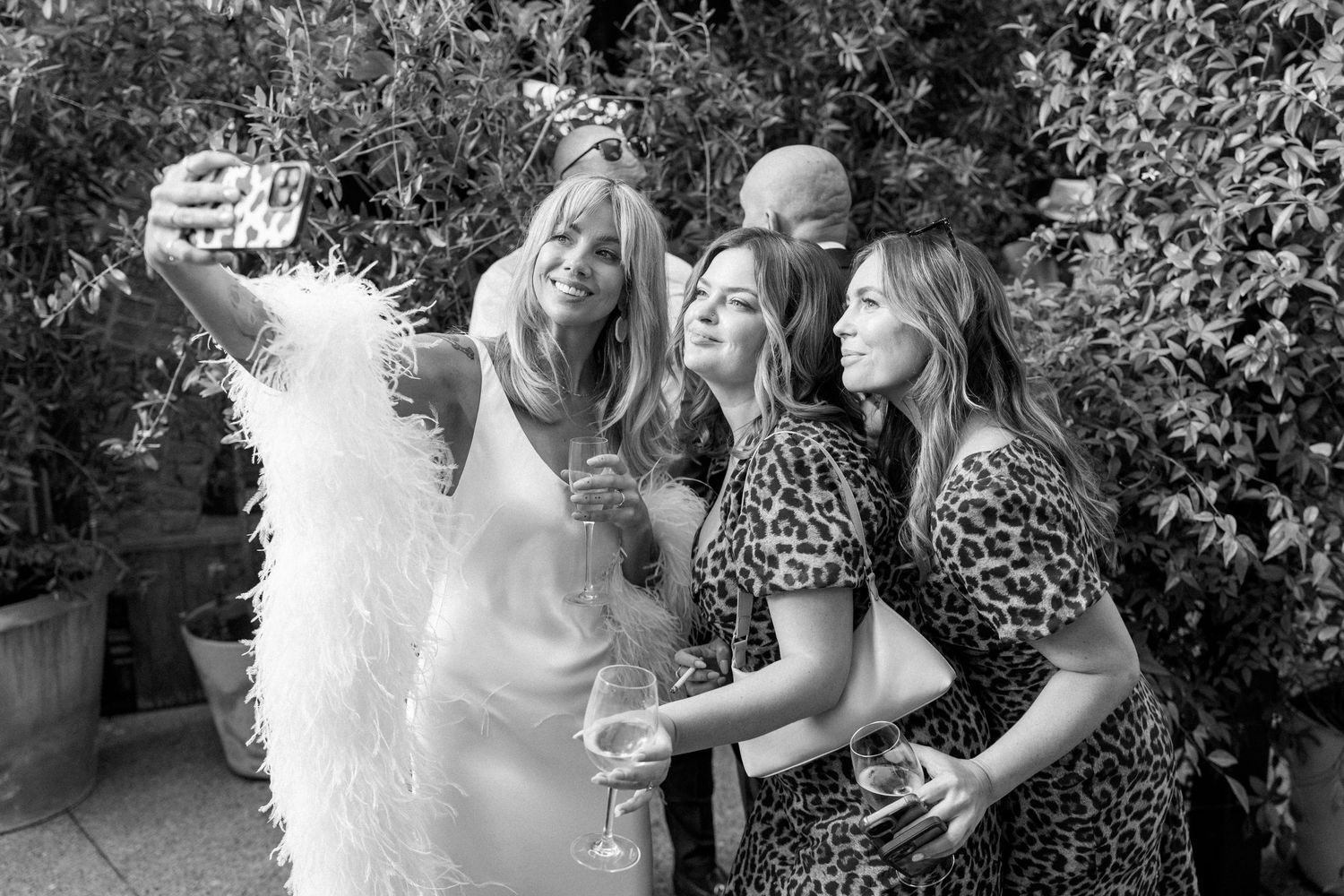 Black and white photo of wedding guests in leopard print dresses celebrating with the bride in feathers.