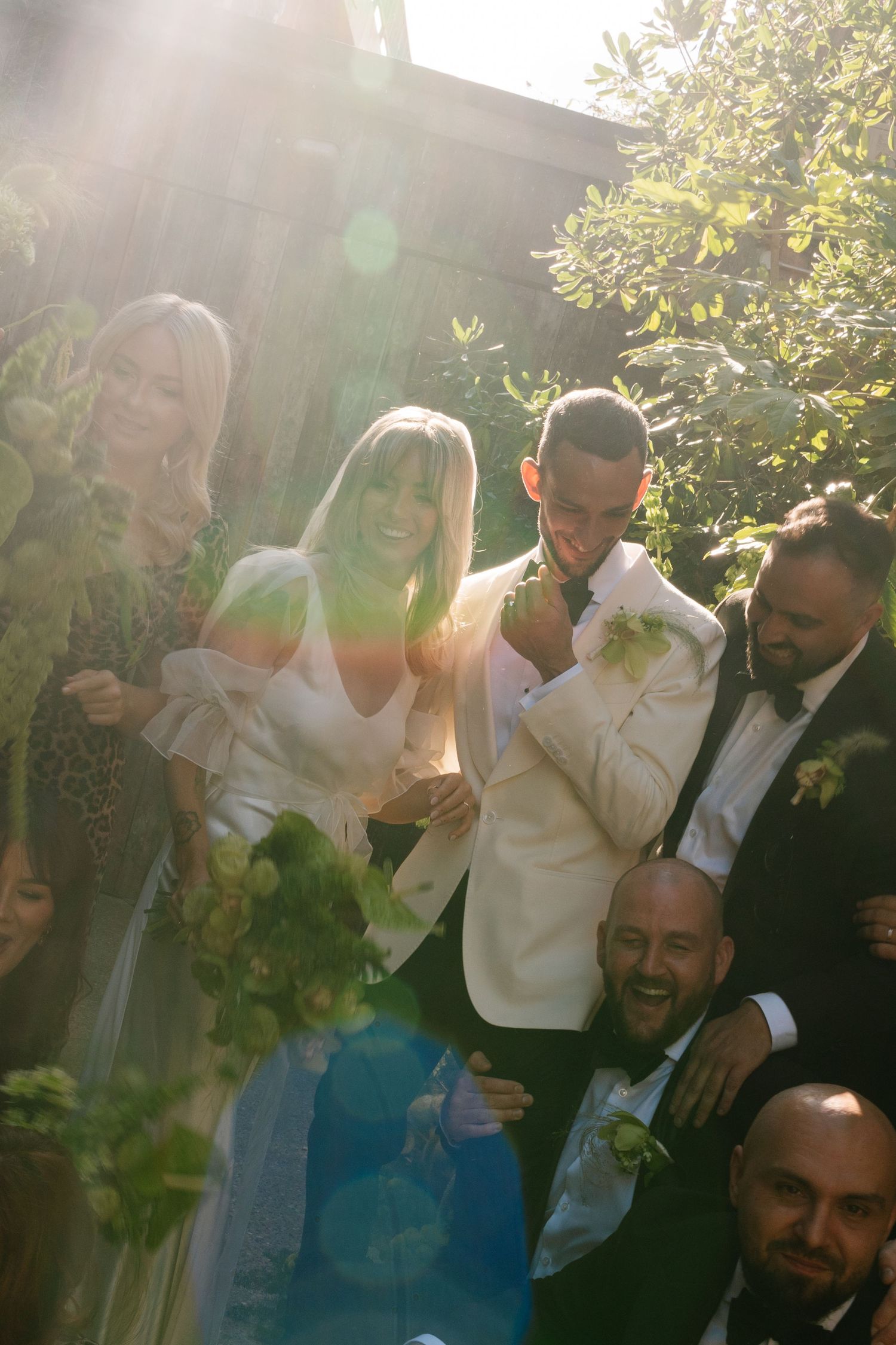 Wedding celebration outdoors with sunlight streaming through trees and foliage.