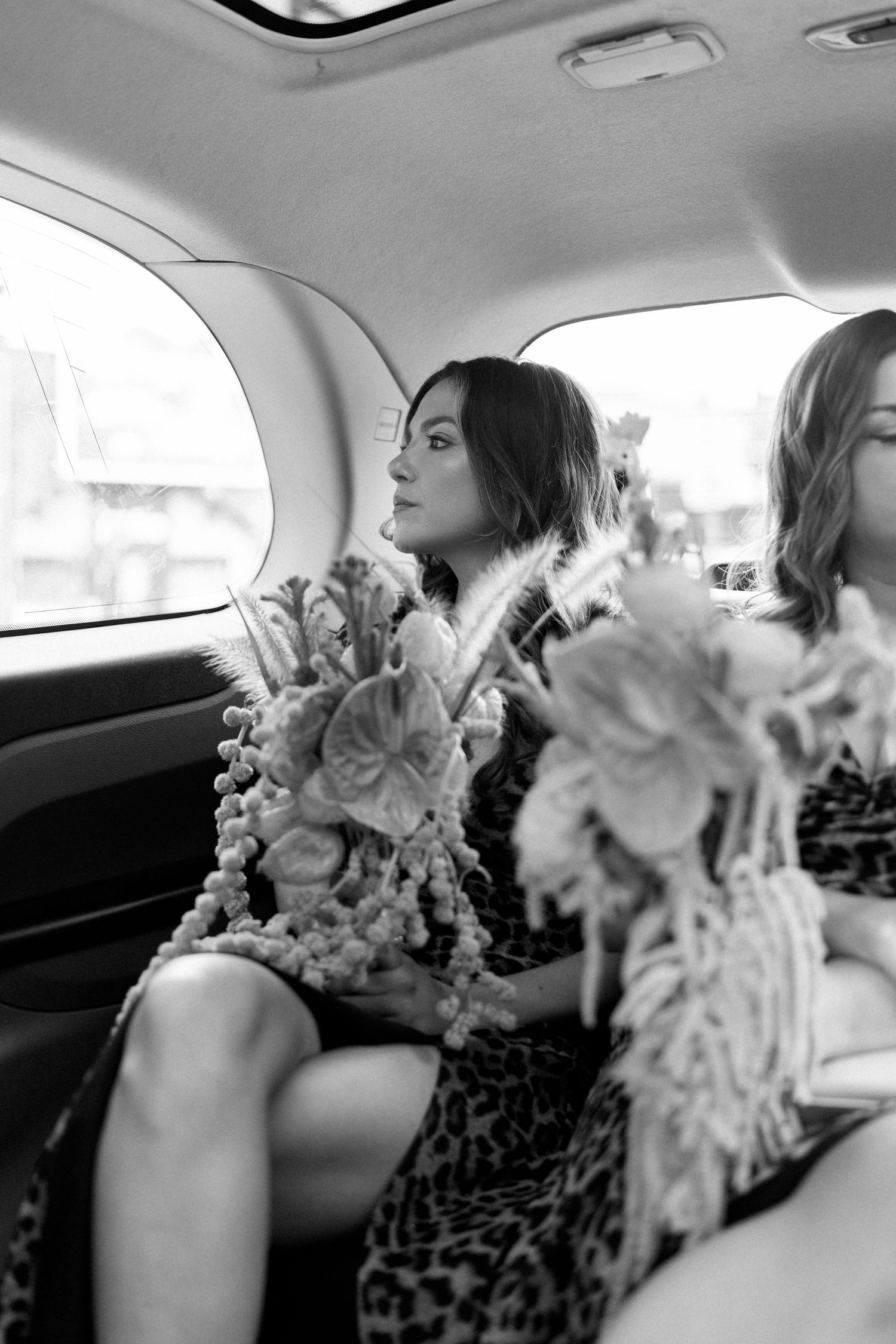 Black and white photo of guests in formal attire sitting in a car with floral decorations.