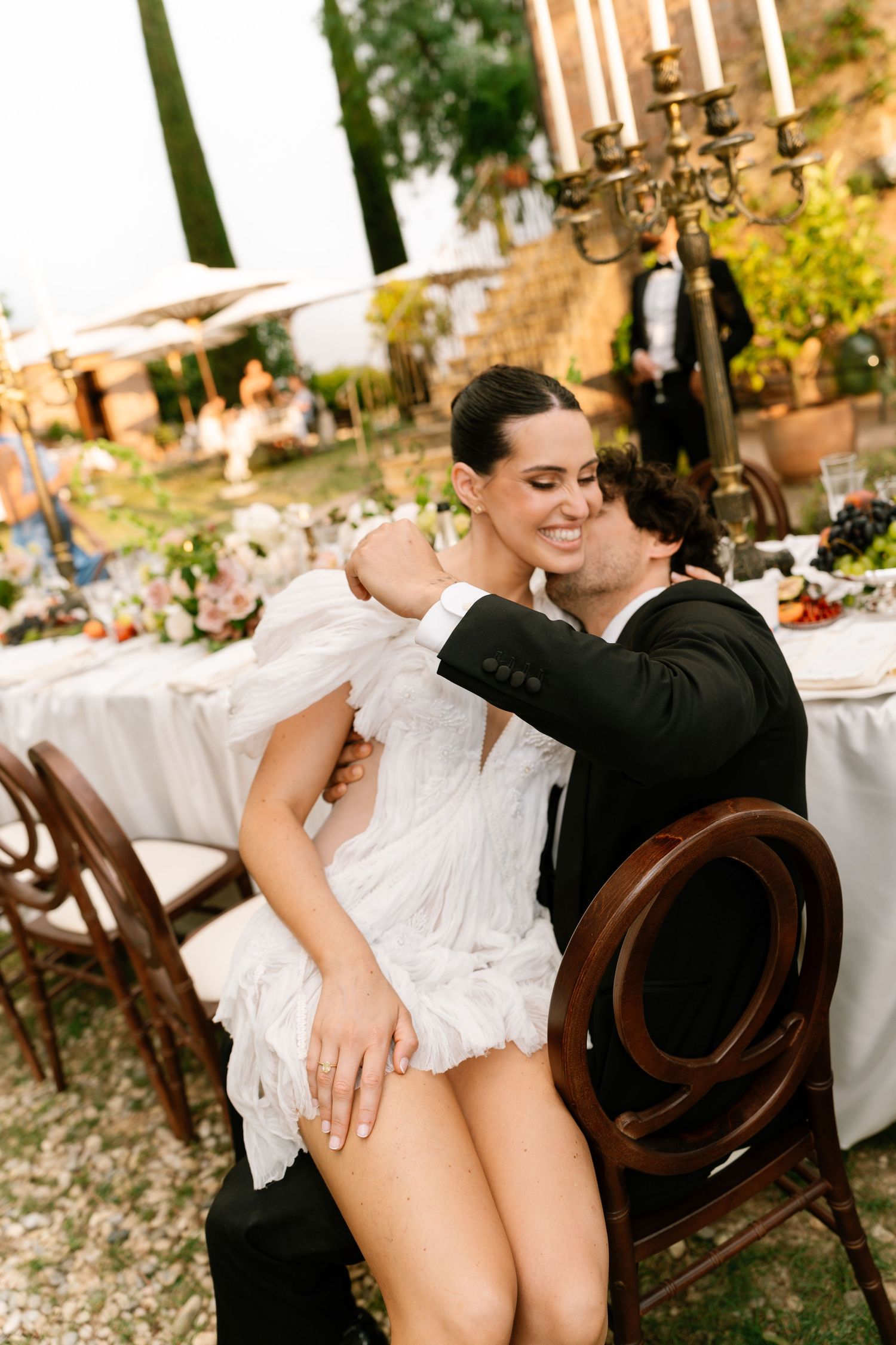 Playful wedding reception moment at an outdoor garden dinner table.