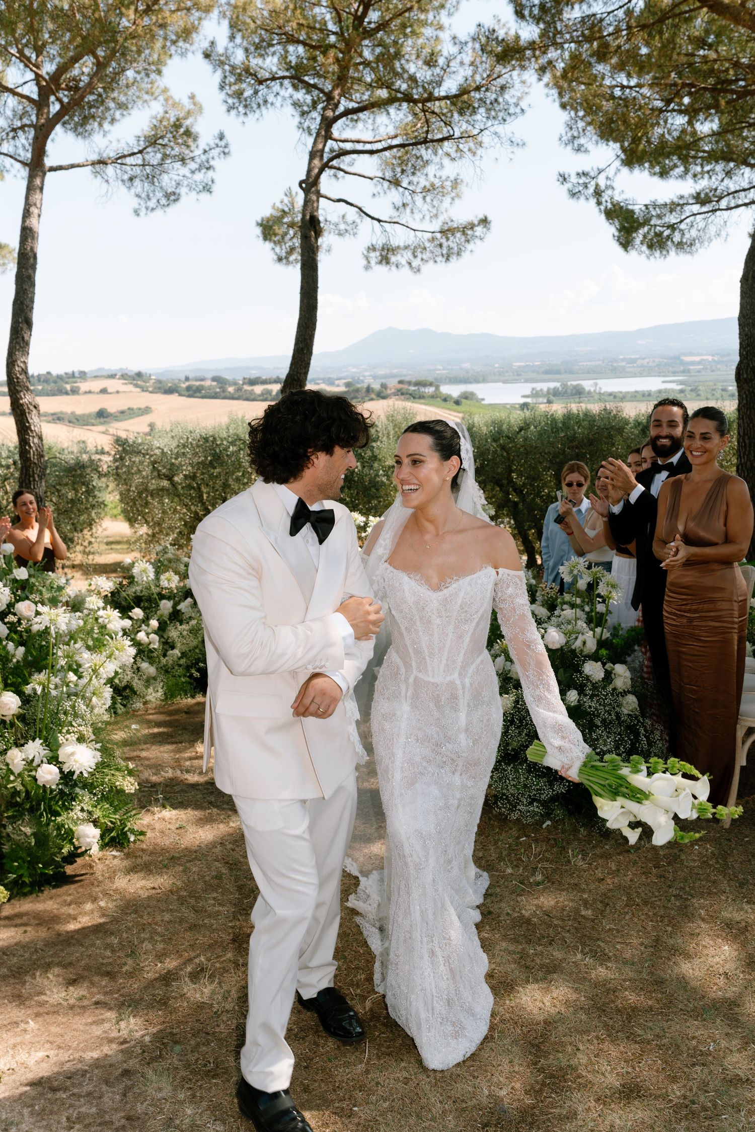 Wedding party walking along a scenic path lined with pine trees in Tuscany.