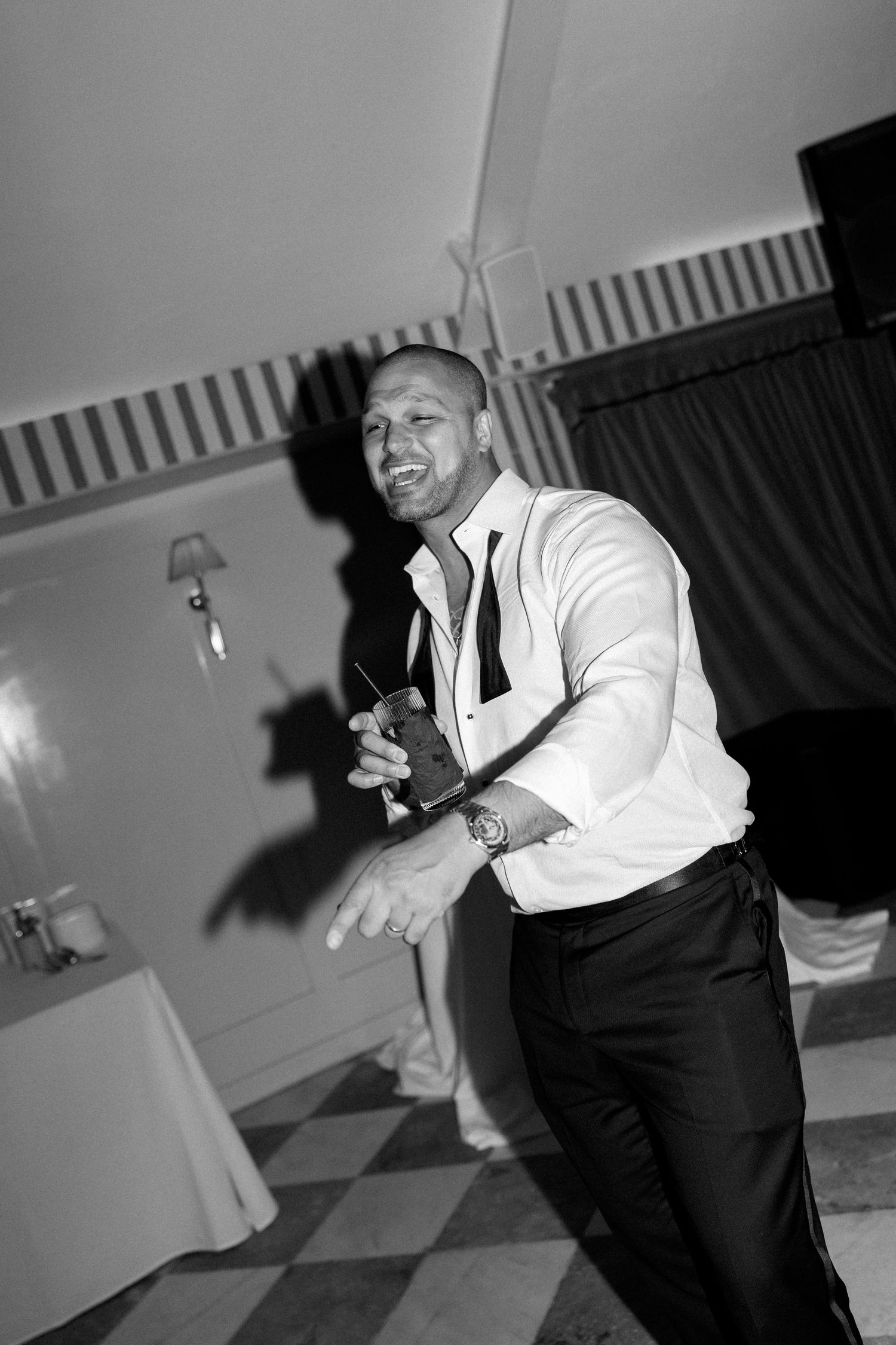 Black and white photo of a smiling man in white shirt and tie dancing at a wedding reception.