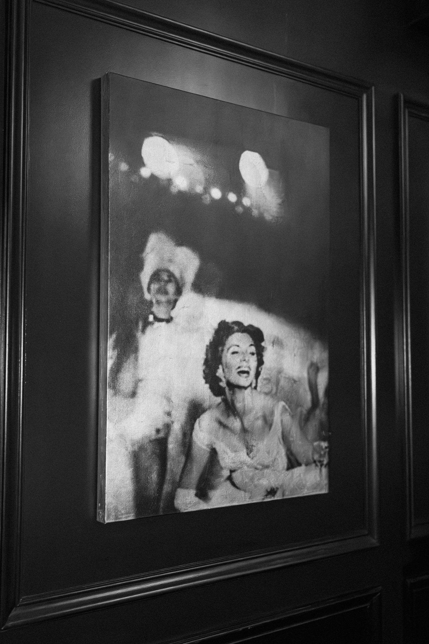 Black and white framed photograph of a glamorous woman laughing at a formal event, displayed on a dark wall.