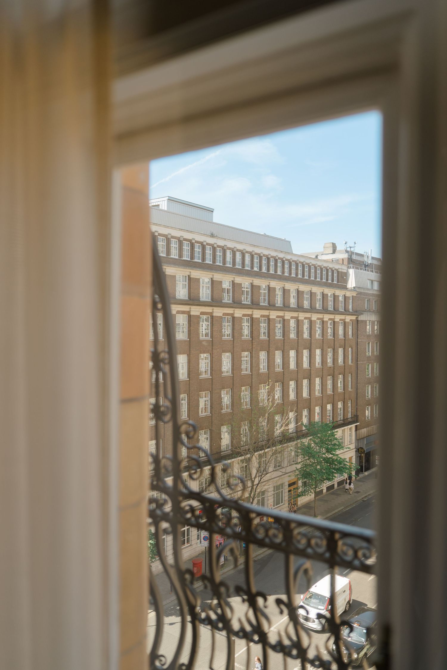Sunlit view through an open window of a grand brick building on a city street.