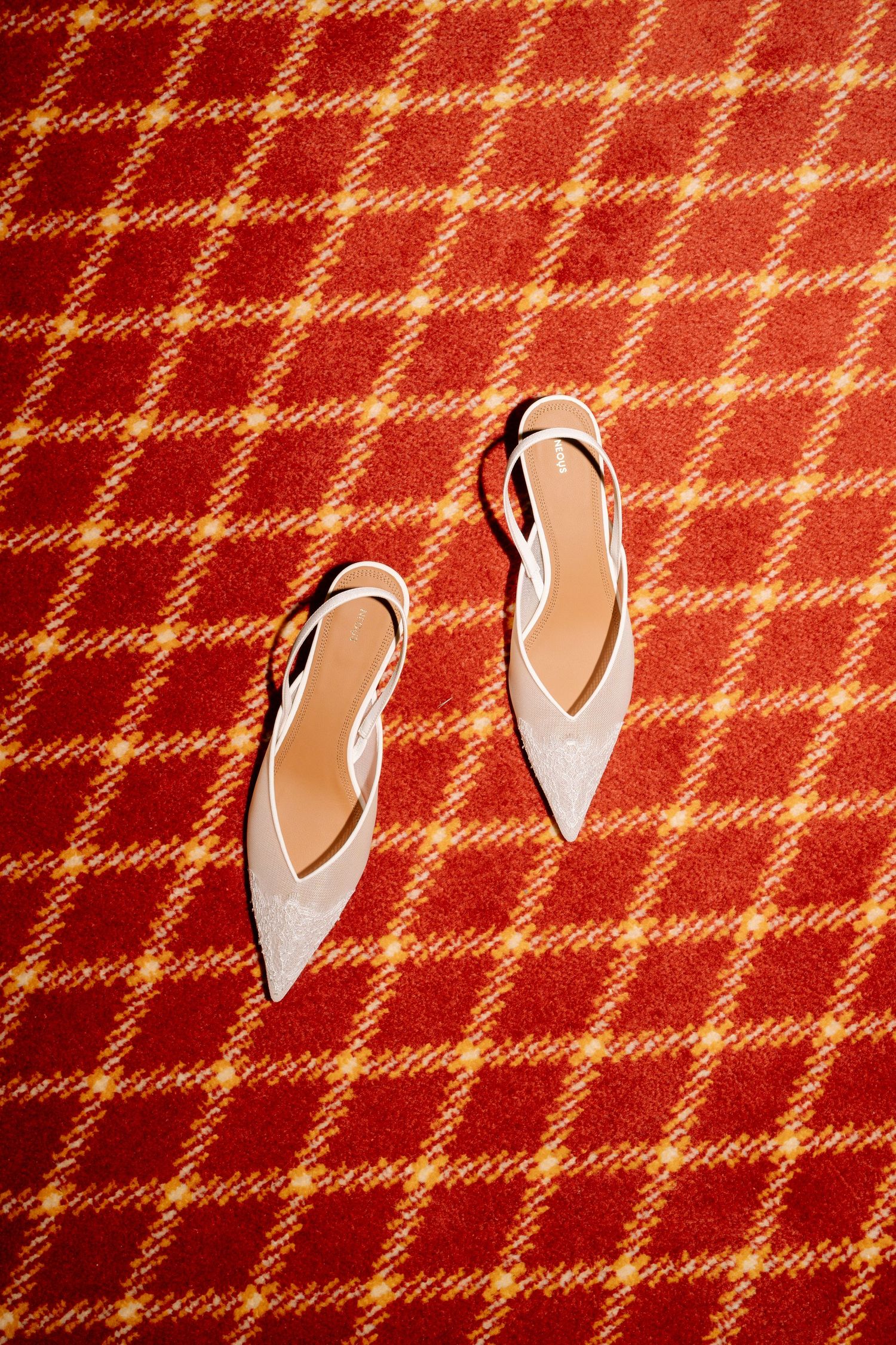 White bridal shoes arranged on red and cream plaid textile background.