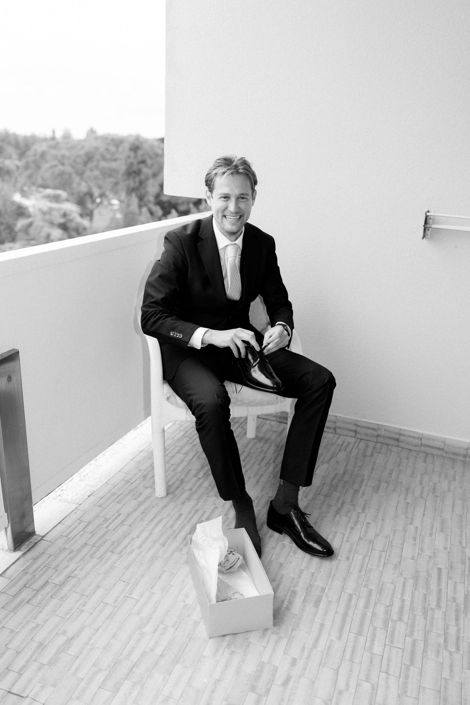 Person in formal suit sitting on outdoor balcony or deck.