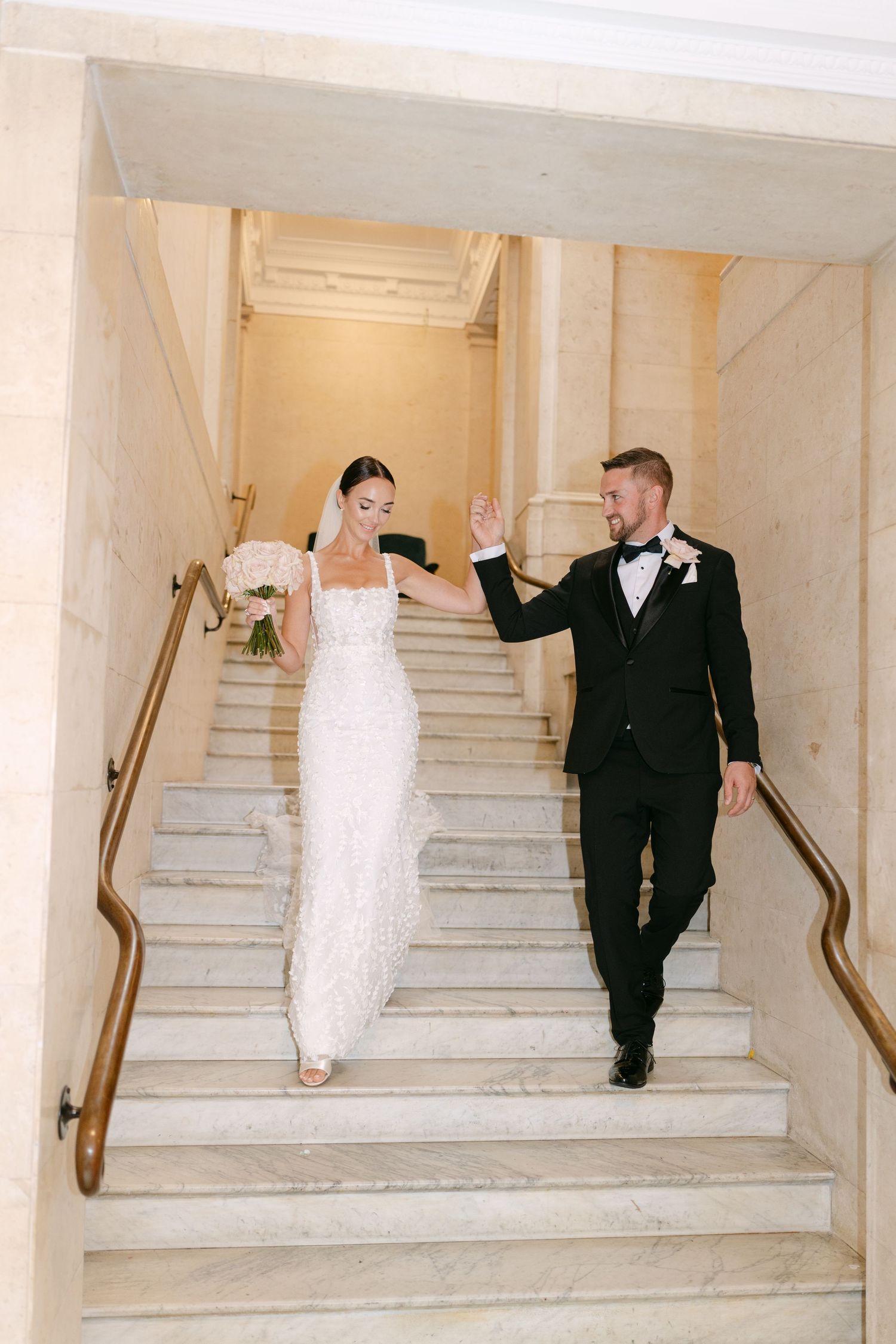 Newlyweds create fun photo sequence on grand white marble staircase.