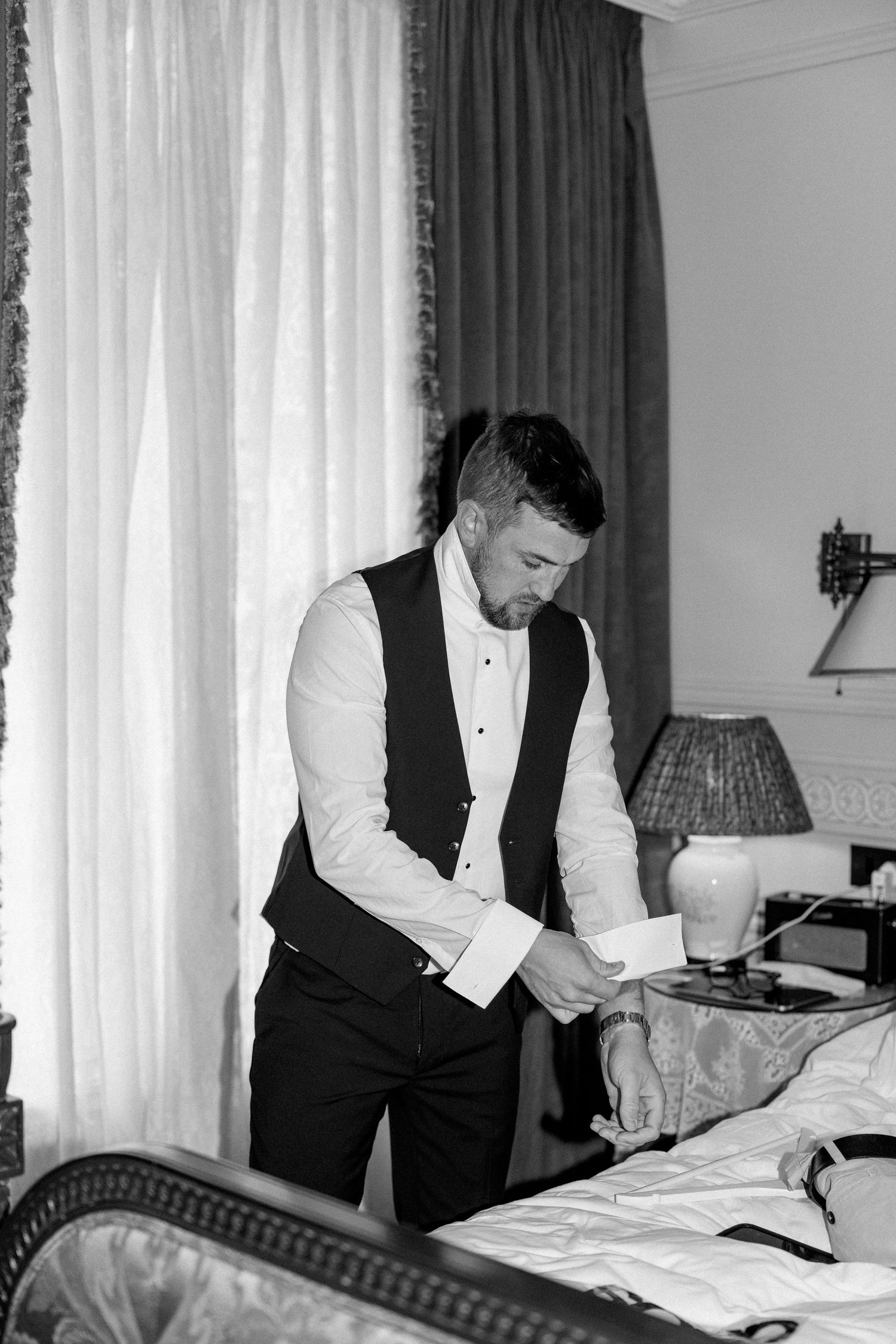 A person in formal attire adjusts their sleeve cuff while getting dressed in a hotel room.