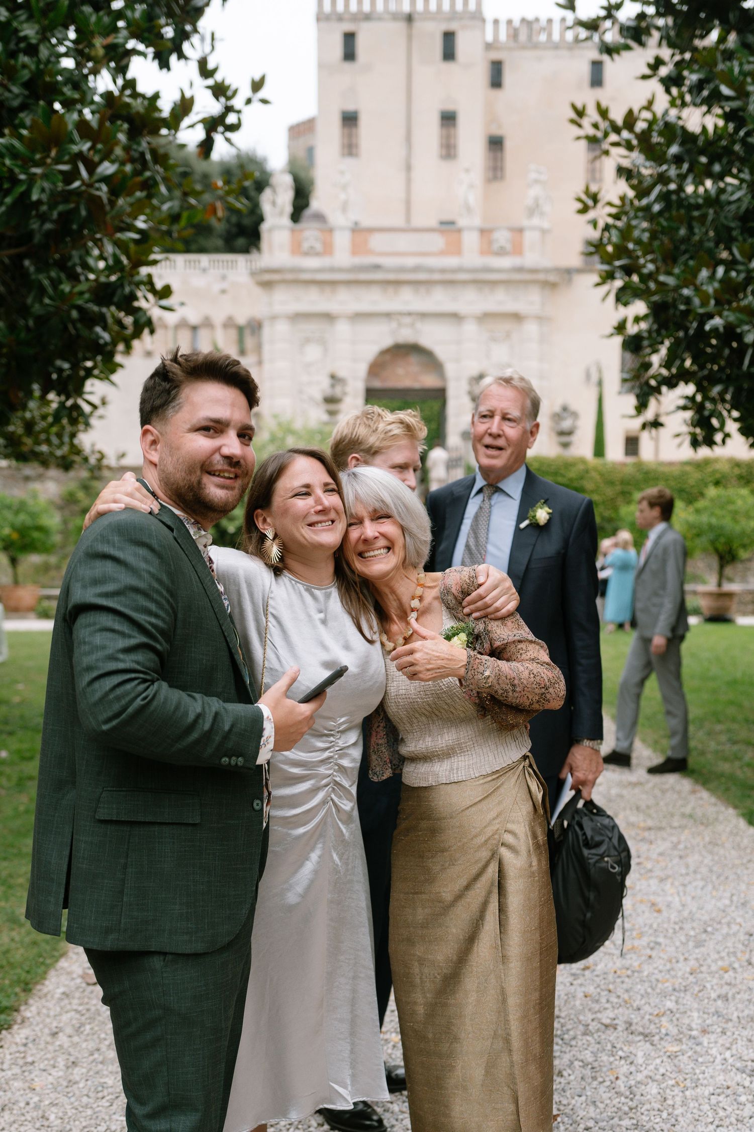 Wedding guests gather for a celebratory photo in front of a majestic European-style castle.