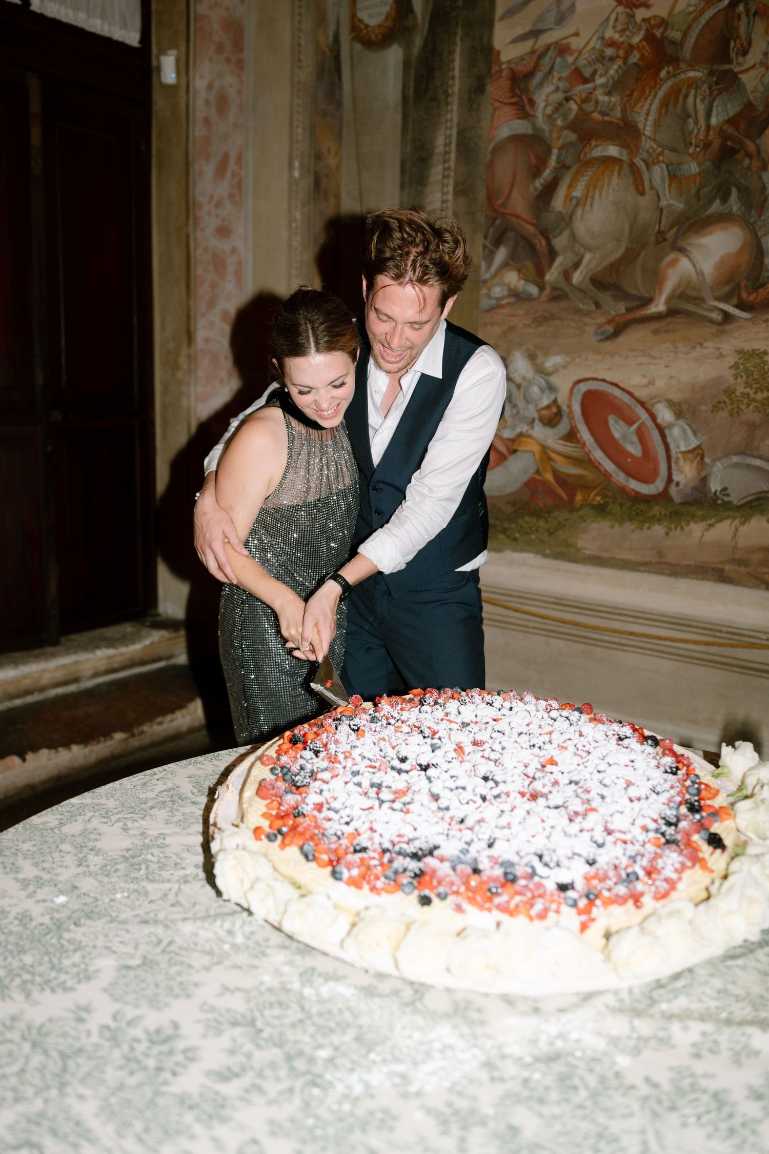 A couple cuts into a berry-decorated cake at their celebration.