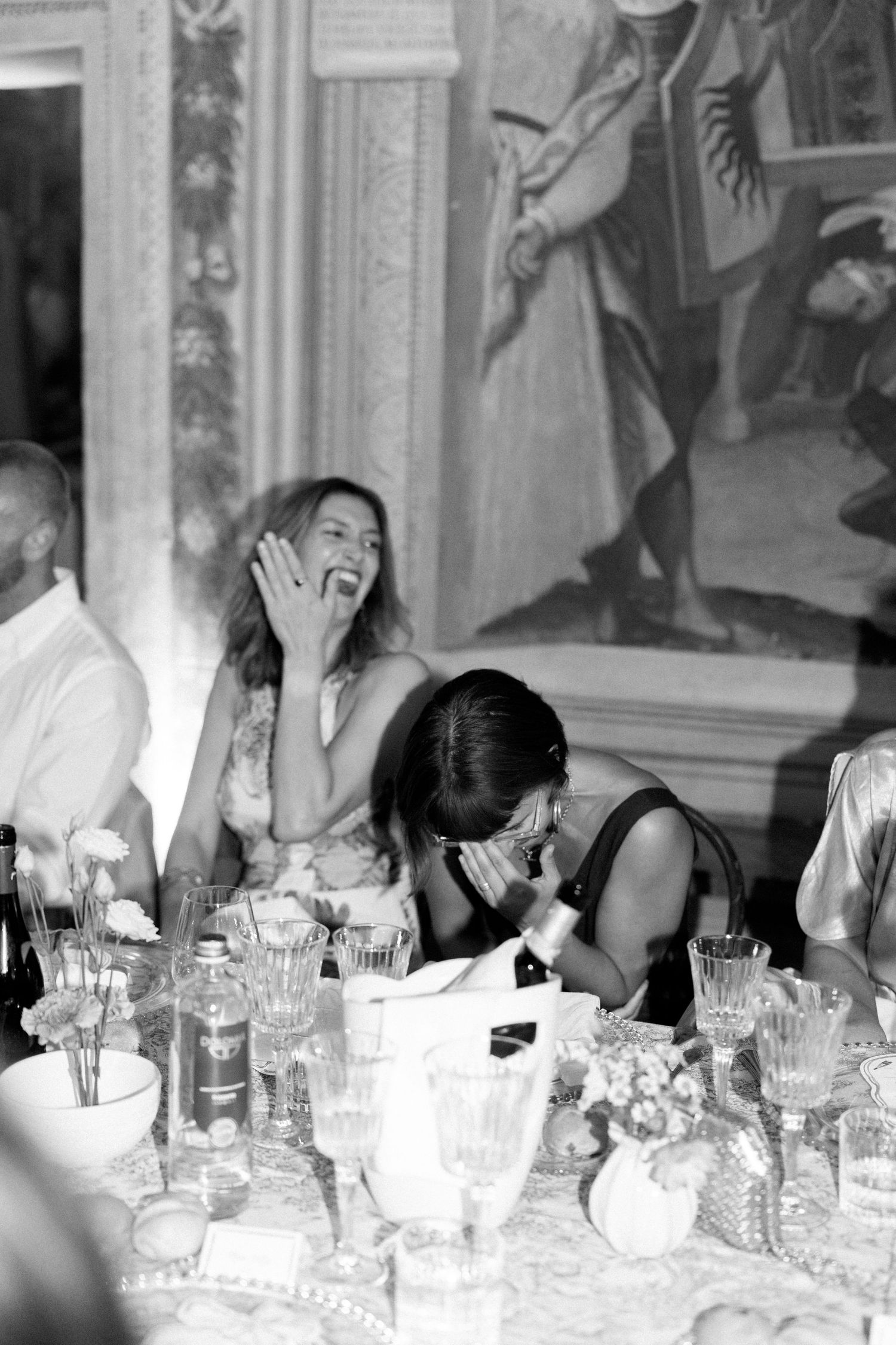 Joyful dinner party scene with guests sharing laughs around a formal dining table.