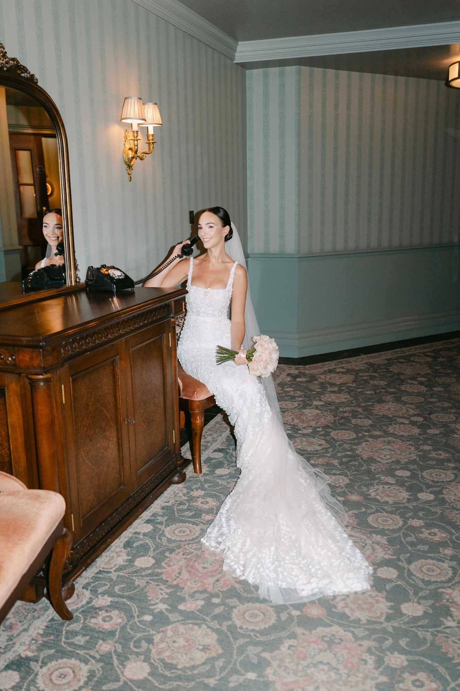 Bride in fitted lace gown poses elegantly against wooden decor in hotel hallway.