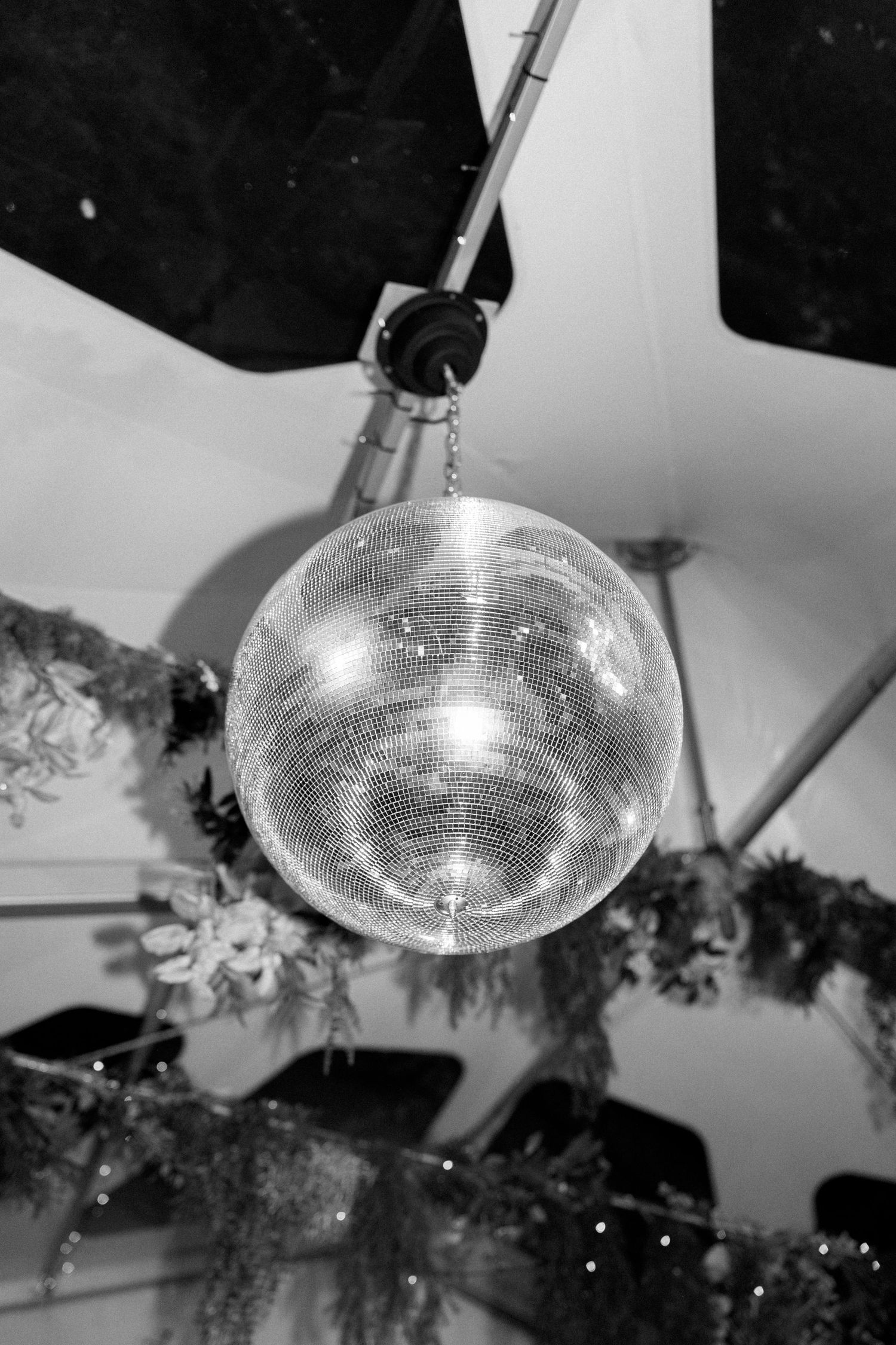 Disco ball hanging from ceiling with greenery decorations at wedding reception.