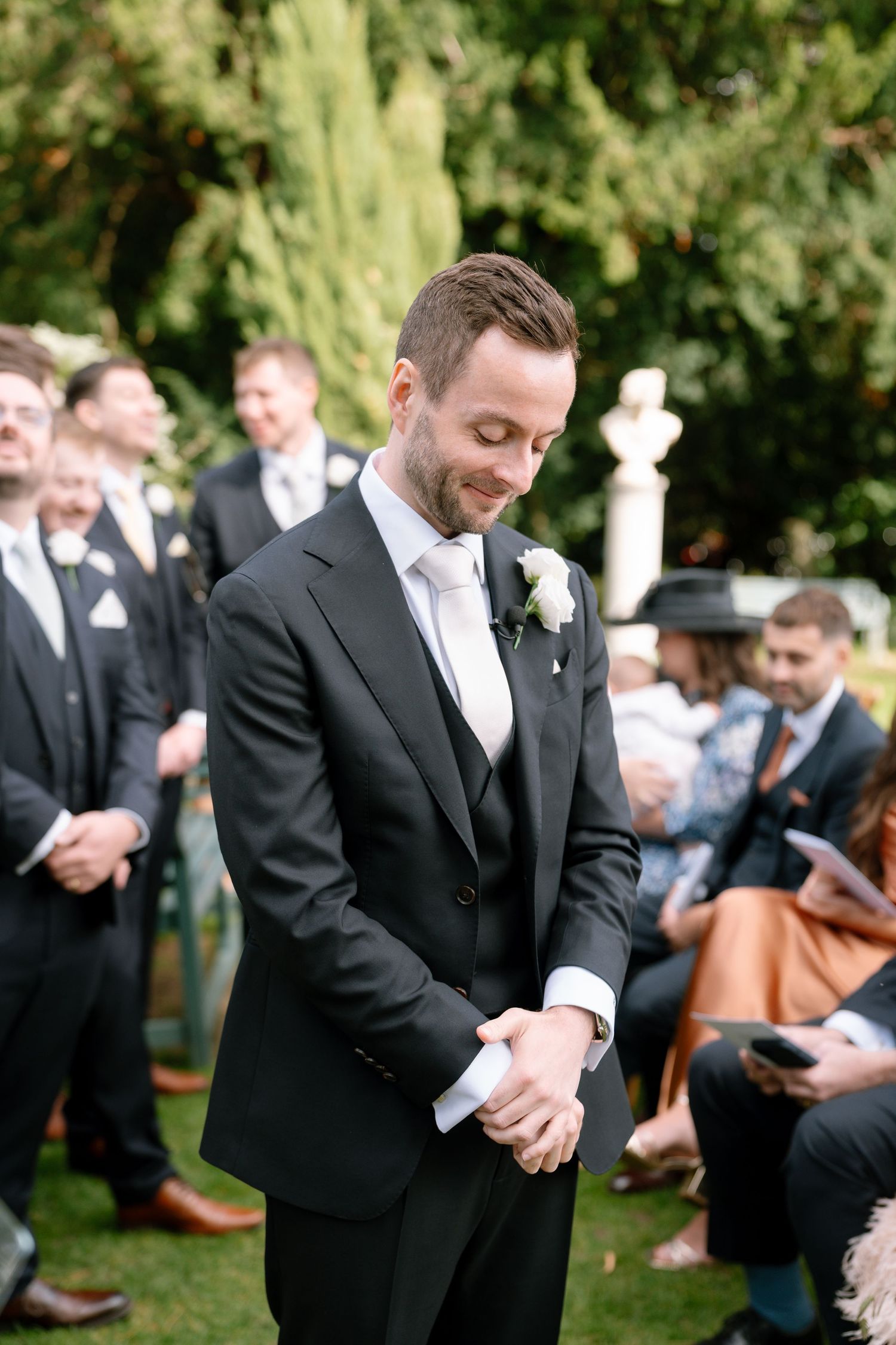 Wedding attendees in formal attire gathered on garden lawn.