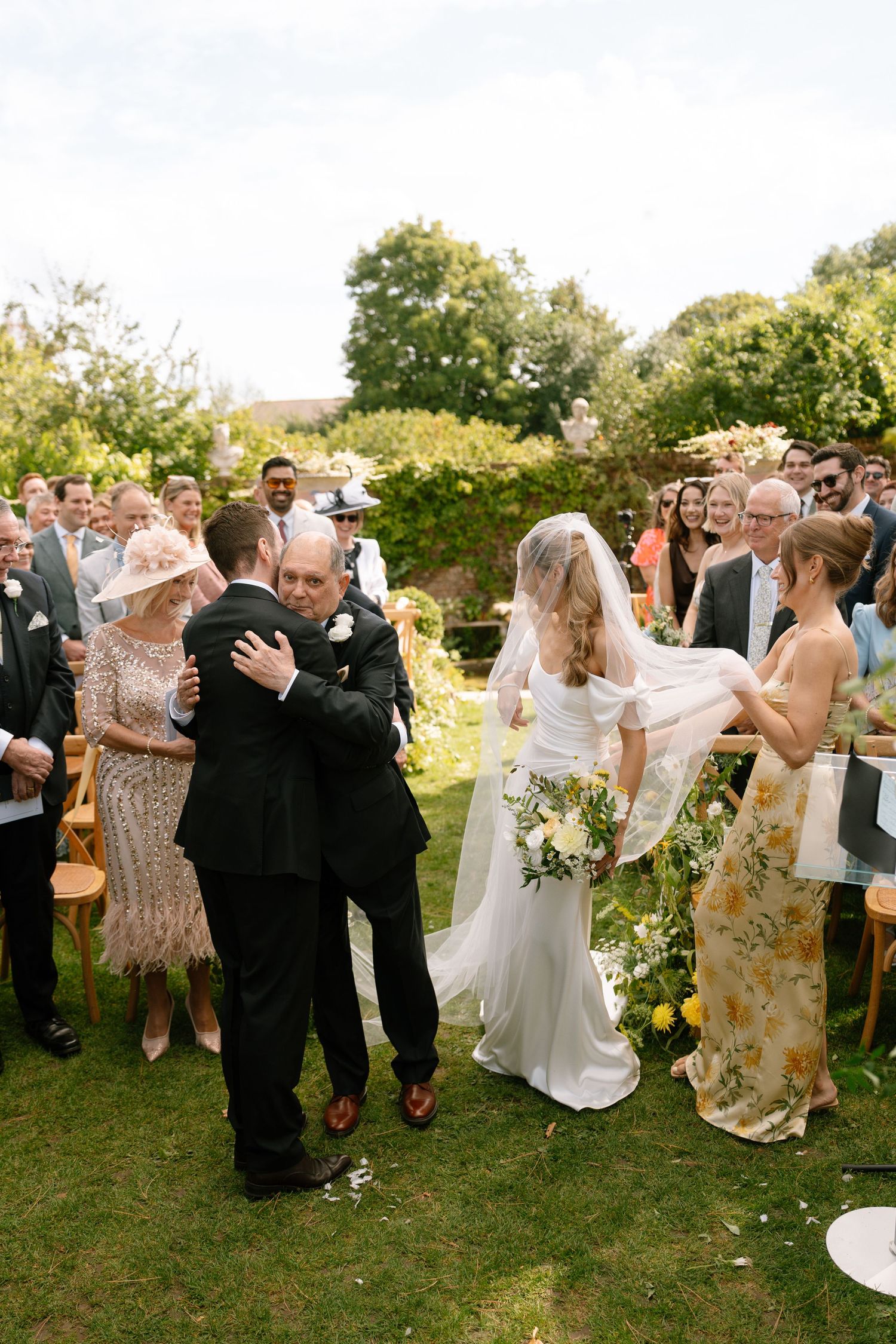 Wedding guests dance and celebrate on a grassy lawn during an outdoor garden reception.