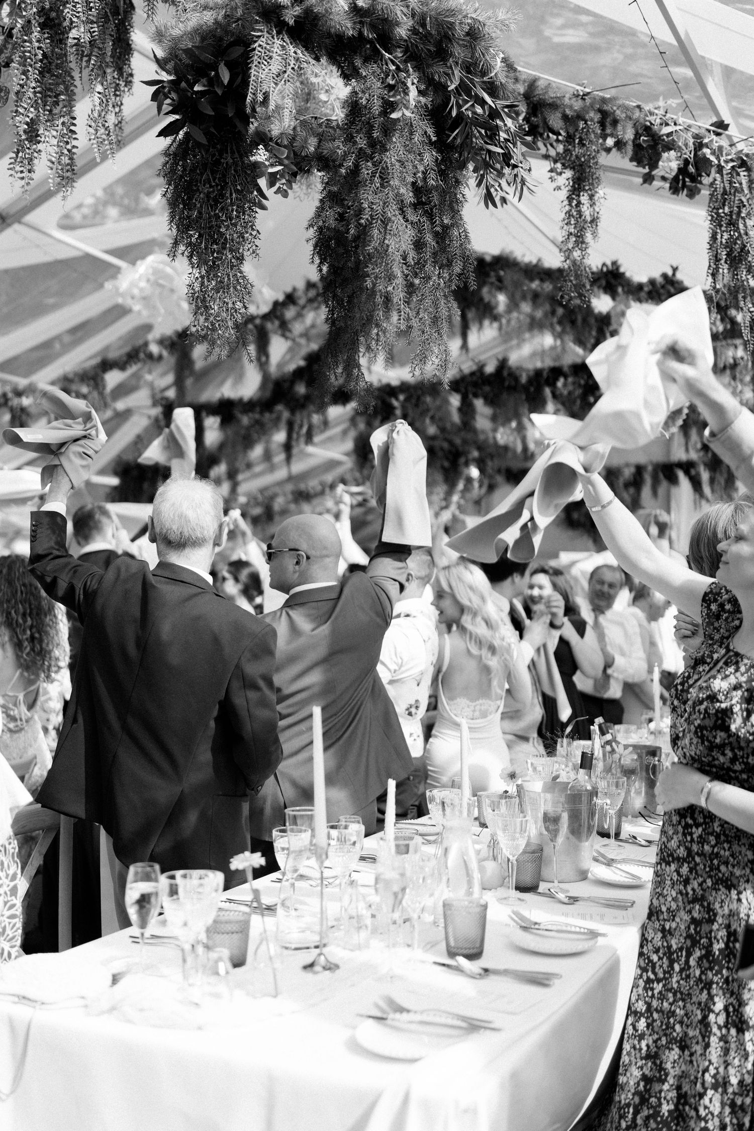 Wedding guests standing and waving napkins during a celebration at an elegantly decorated table setting.