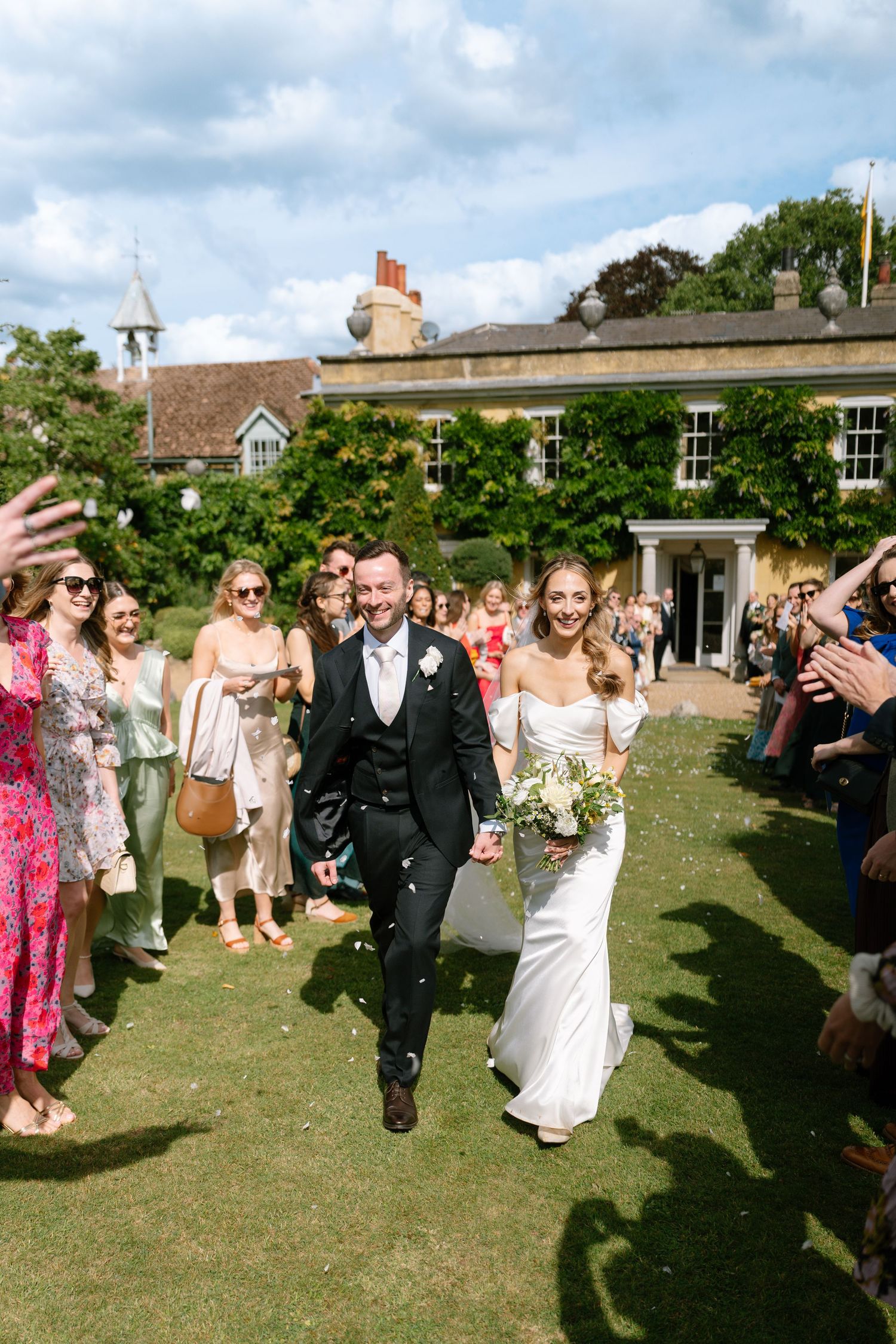Wedding celebration on a sunny lawn with guests throwing confetti at the newlyweds.