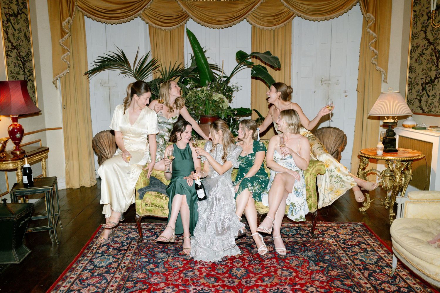 Wedding celebration with guests in formal attire seated on luxurious furniture under gold drapery.
