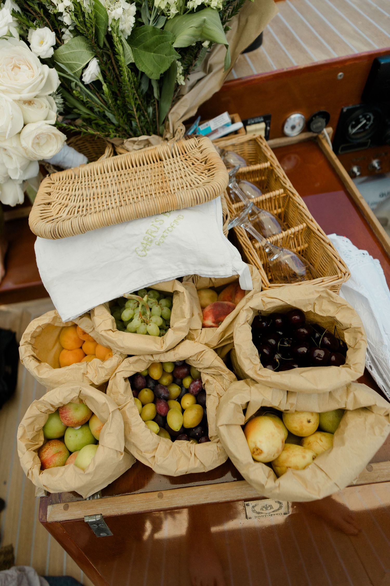 Rustic wedding picnic display with fresh fruits in paper bags, wicker baskets, and white roses.