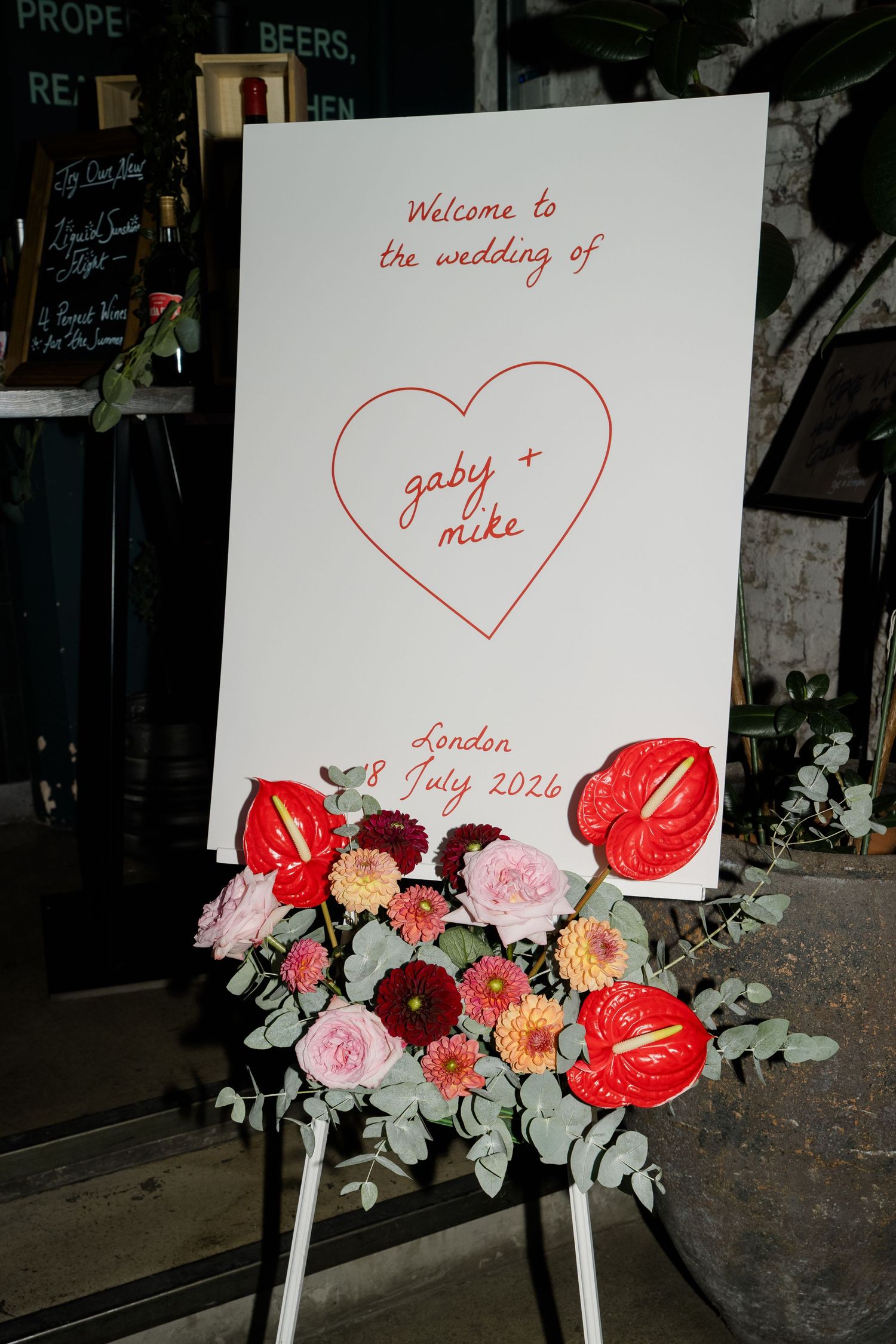 Wedding welcome sign for Gaby and Mike, London, 8 July 2024, decorated with red anthurium and mixed floral arrangement.