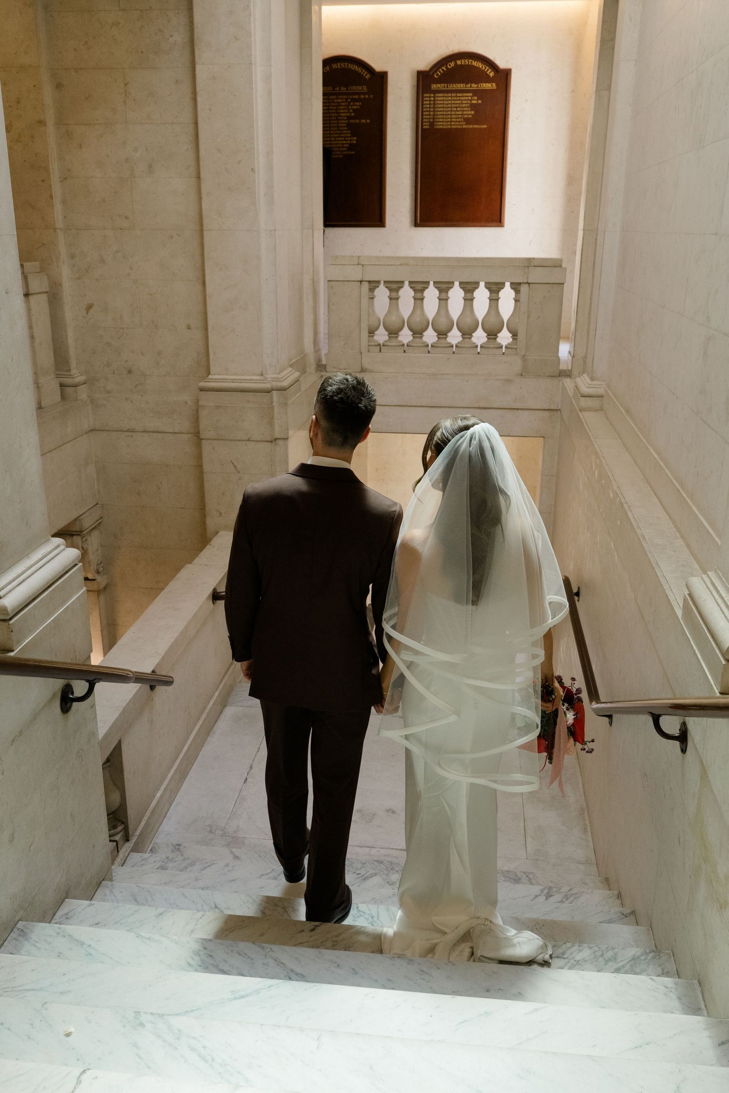 Bride and groom walking up marble stairs in elegant wedding venue.