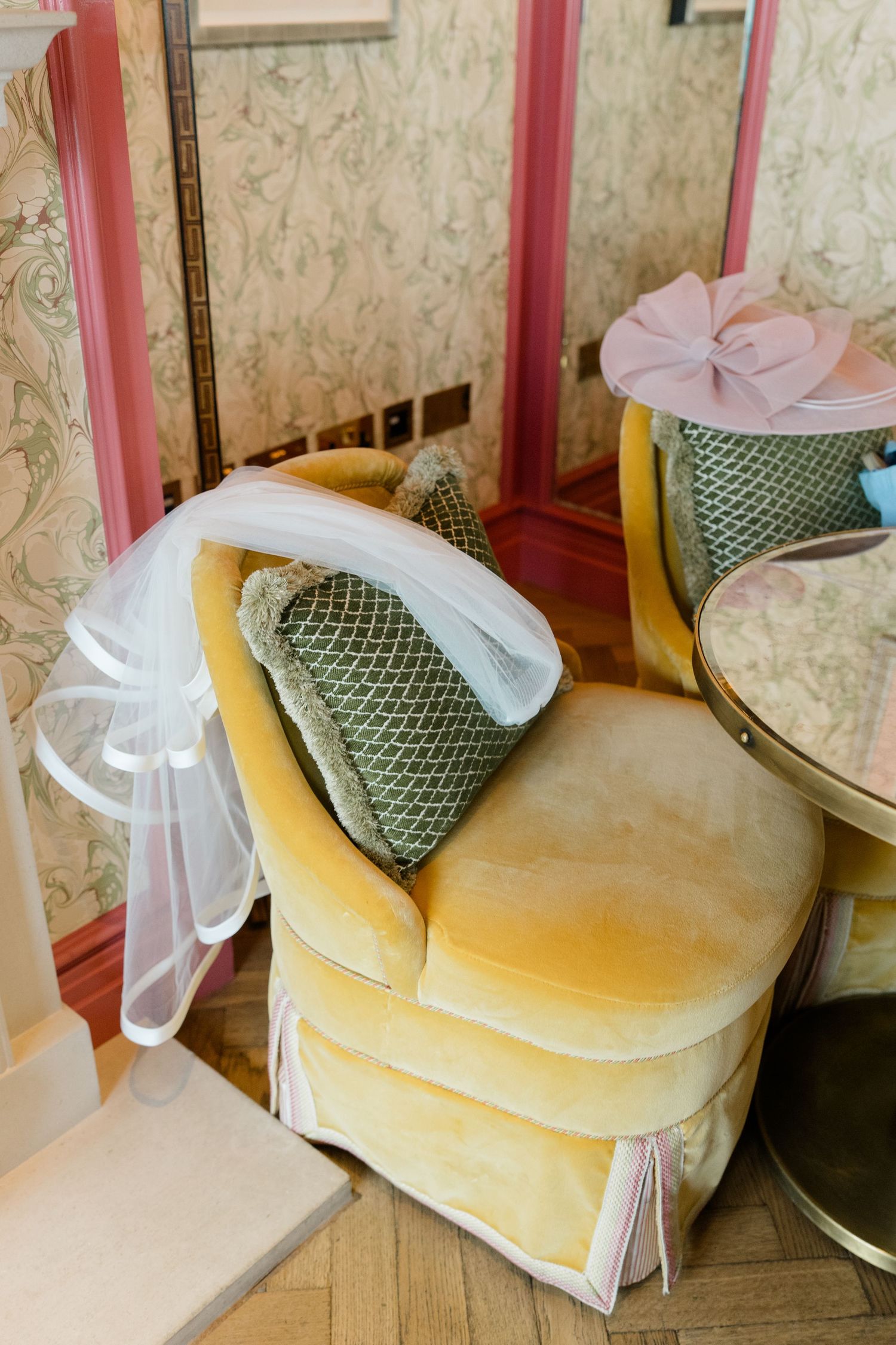 Elegant yellow velvet chair with bridal veil draped over it beside a vanity in a vintage-styled dressing room.
