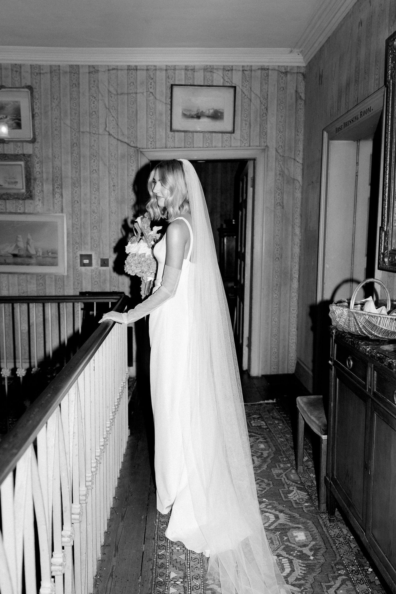 Black and white photo of bride in veil holding bouquet at staircase landing.