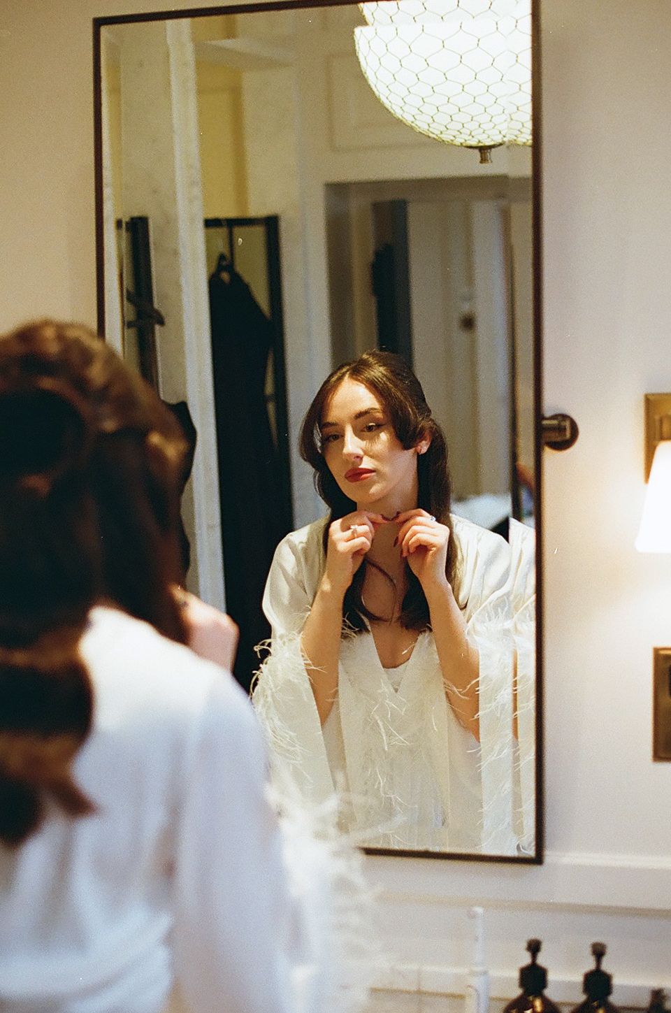 Multiple reflections in mirrors show a person in a white top styling their dark hair in an elegant interior setting.