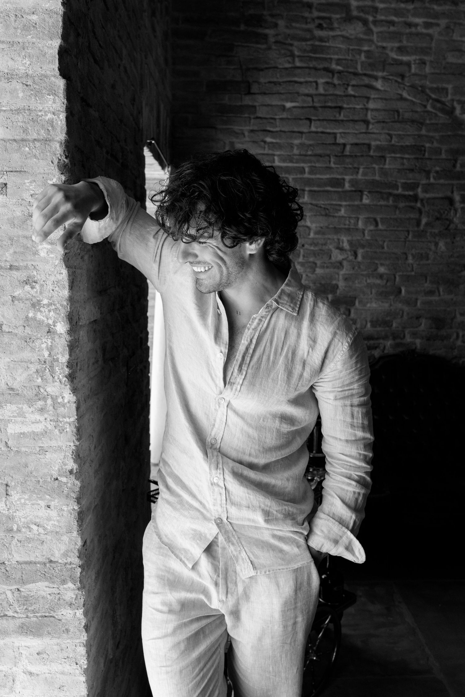 Four black and white photos show a figure in white clothing leaning against a brick wall in dramatic lighting.