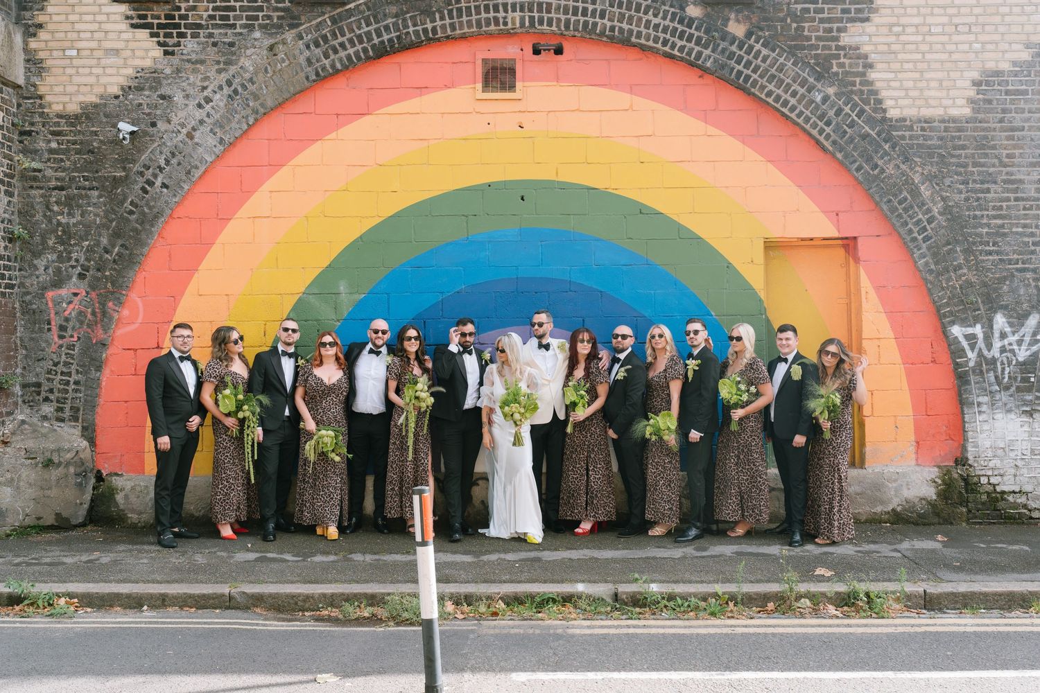 Large wedding party group photo in front of vibrant rainbow mural.